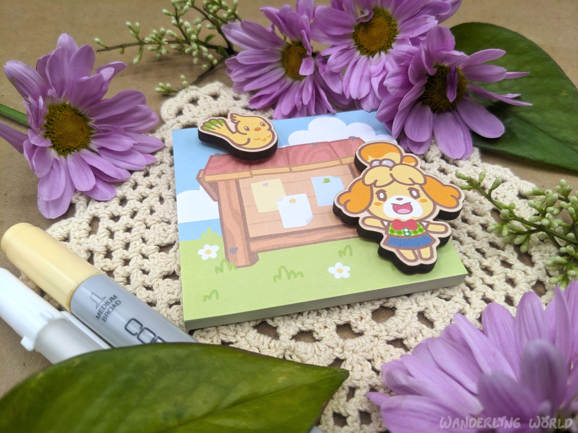 Photo of a memo pad with two wood magnets sitting on top of it. The image on the memo pad is a cute outdoor bulletin board. The Isabelle magnet stands next to the bulletin board waving and a little yellow bird magnet perches on top the bulletin board.