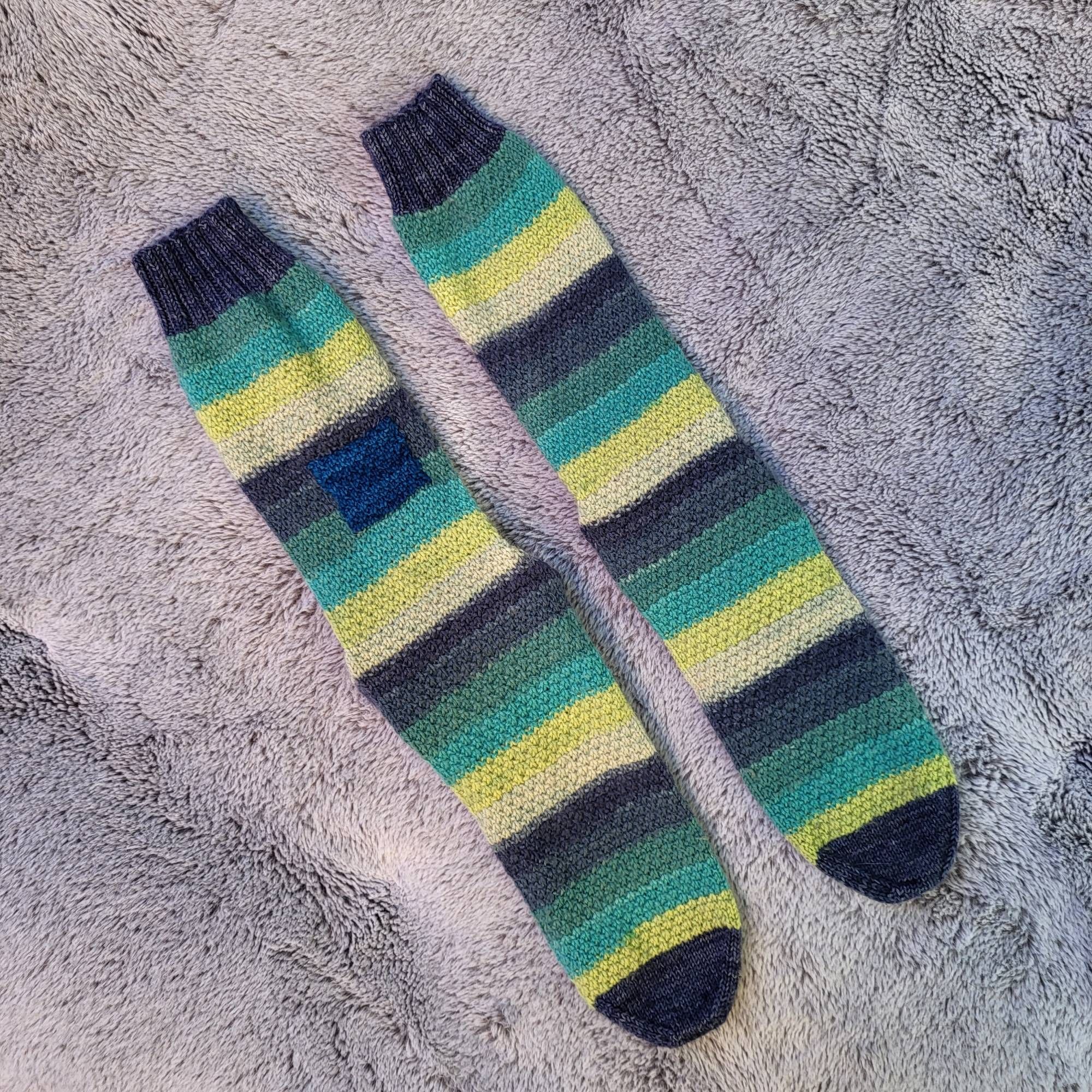 A pair of blue and green striped socks patched with a blue square.