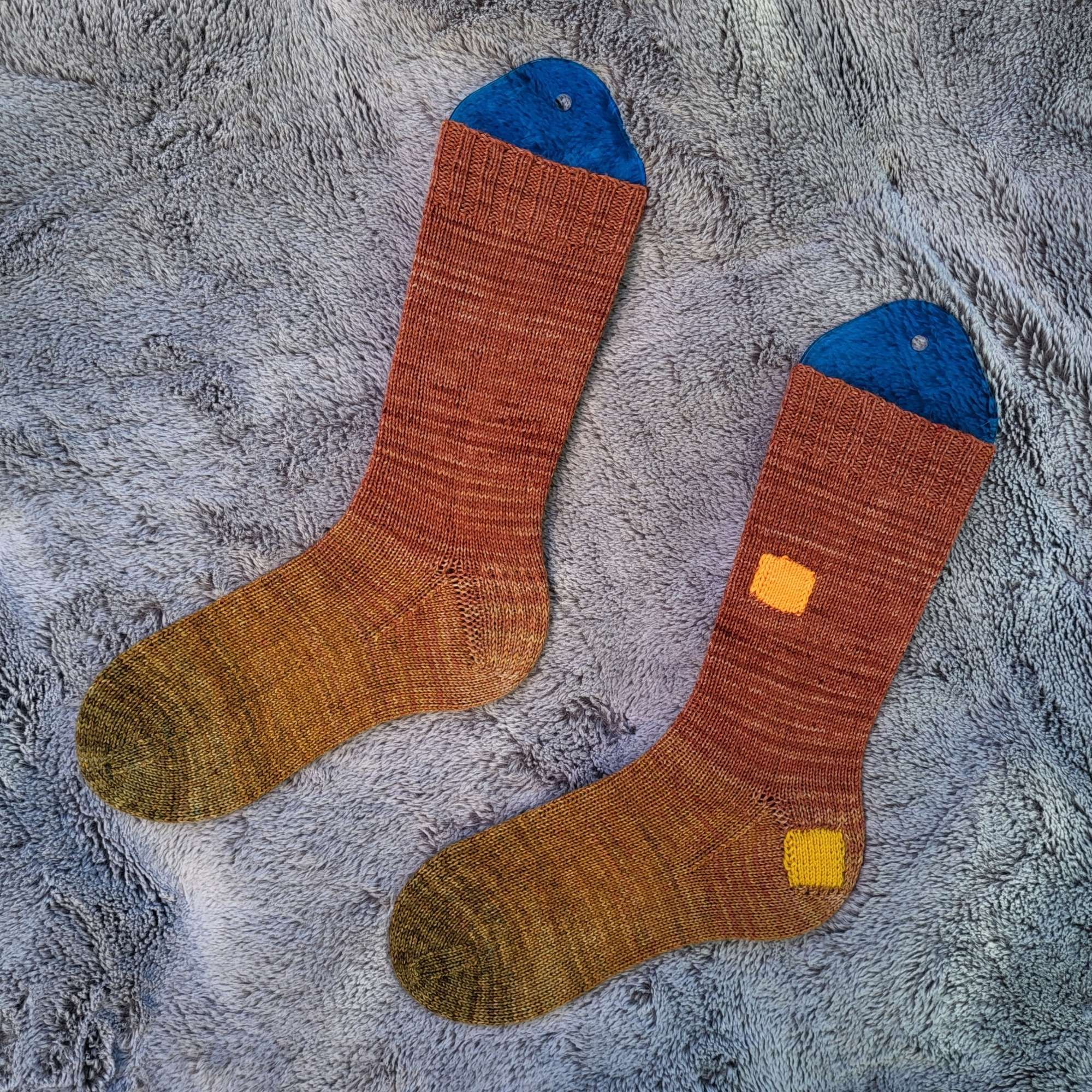 A pair of orange socks patched with orange and yellow squares.