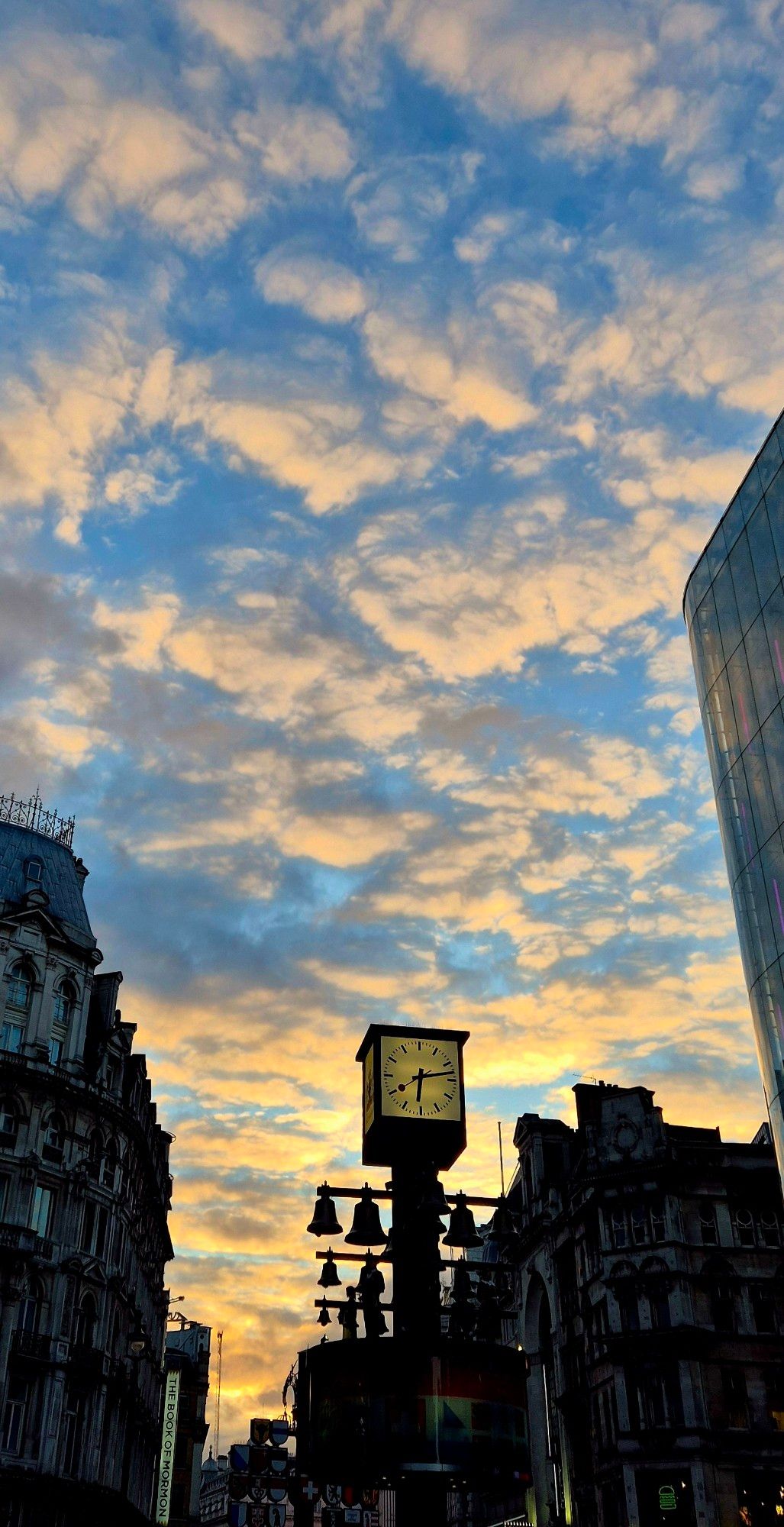 A clock with bells and rooftops with a blue sky and orange sunset-filled clouds