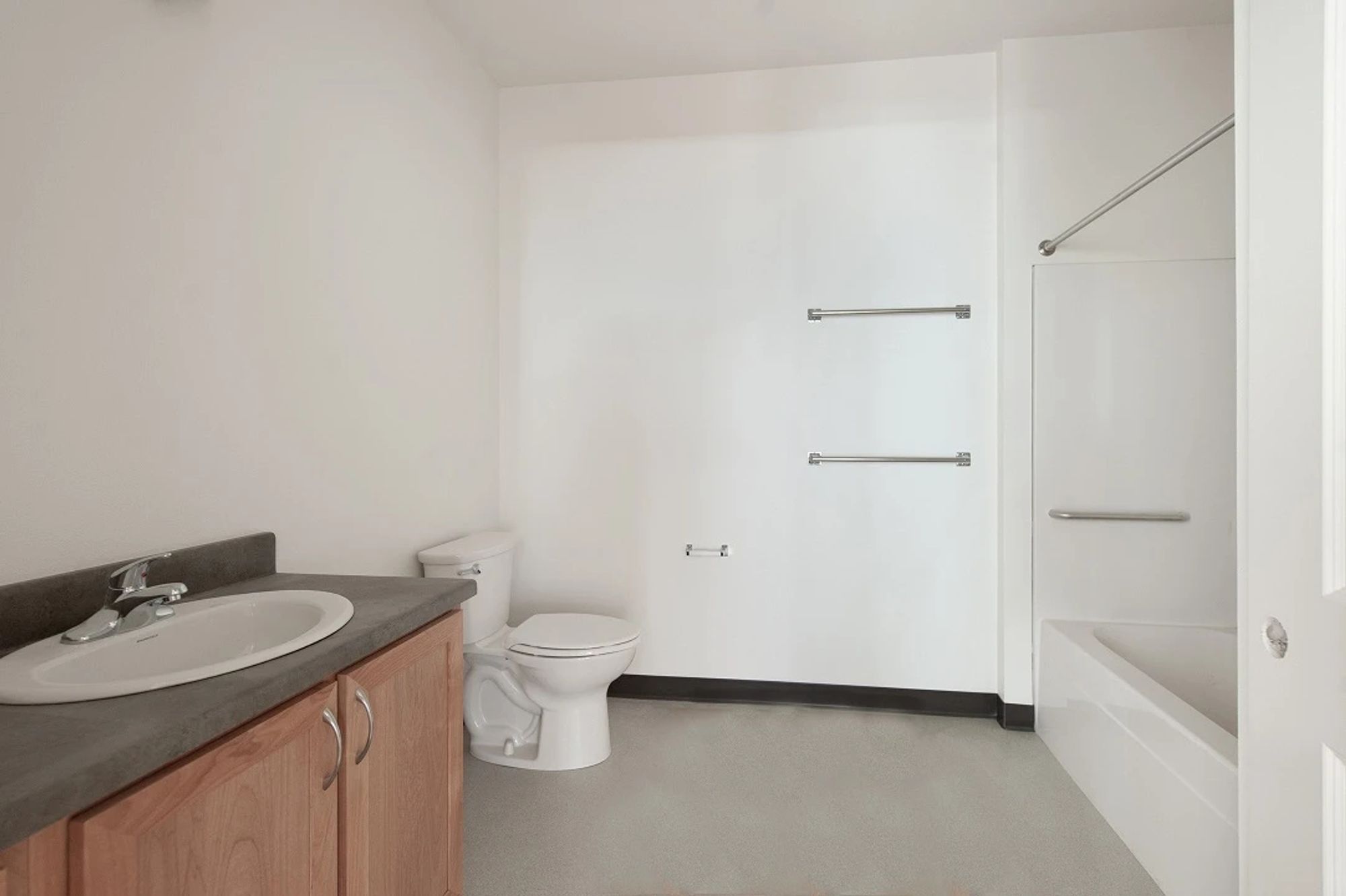 Photo of an "accessible" bathroom. There's no safety bars except inside the tub, and the sink is not accessible because there's enclosed cabinetry beneath it. A wheelchair user couldn't pull up to it or reach it. The wall opposite the sink is positioned in a way that would make pulling a chair in the face the sink impossible. You might be able to pull alongside it sideways, but then you can't wash or anything.