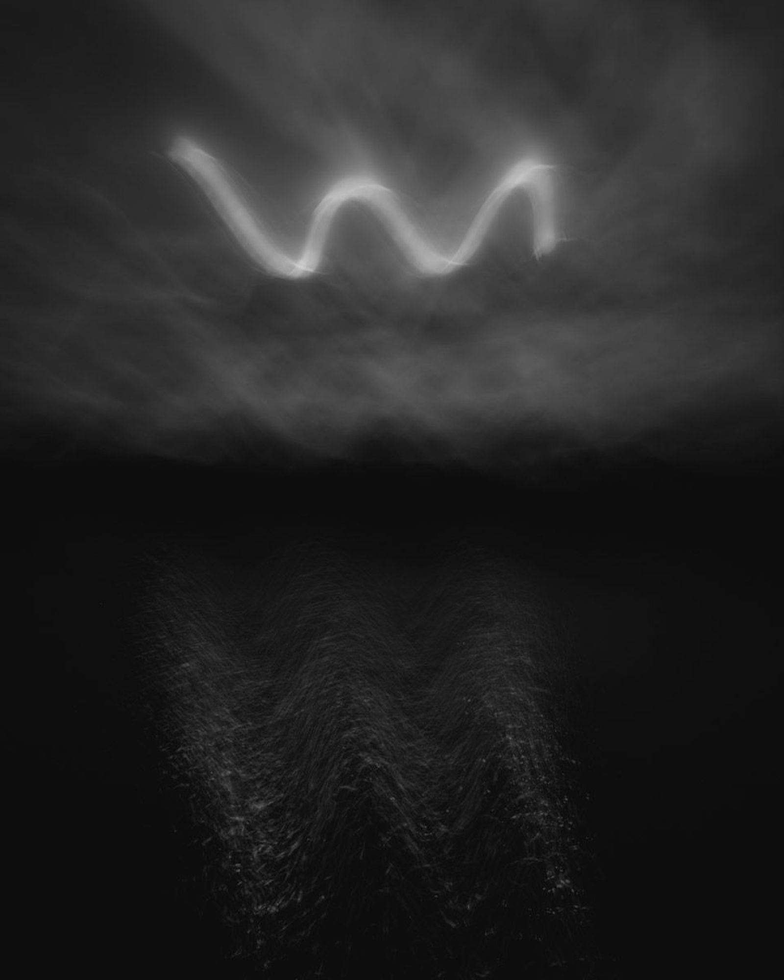 ‘Sine’ is a black and white abstract landscape photograph from the series ‘dark days irl’. A very dark exposure, it uses intentional camera movement to paint with the sun a rough sine like waveform in the sky that’s reflecting shakily and mysteriously below in a rippling body of water. The entire image is dark, blurry and ambiguous with a lake, line of distant trees or hills and clear, graduated sky with sun drawn sine wave. 