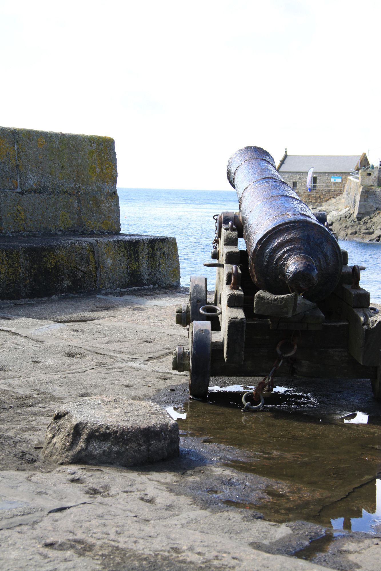 Photo of an age of sail canon on a harbour wall, pointing out to sea, taken from a low angle behind the canon.