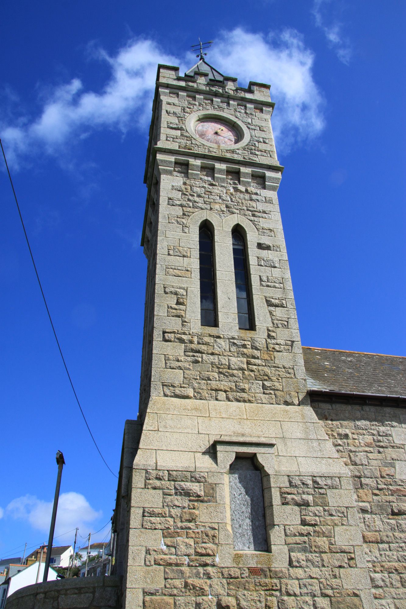 Photo of clocktower in Porthleven harbour, taken from below, looking up into a blue sky with some fluffy cloud.