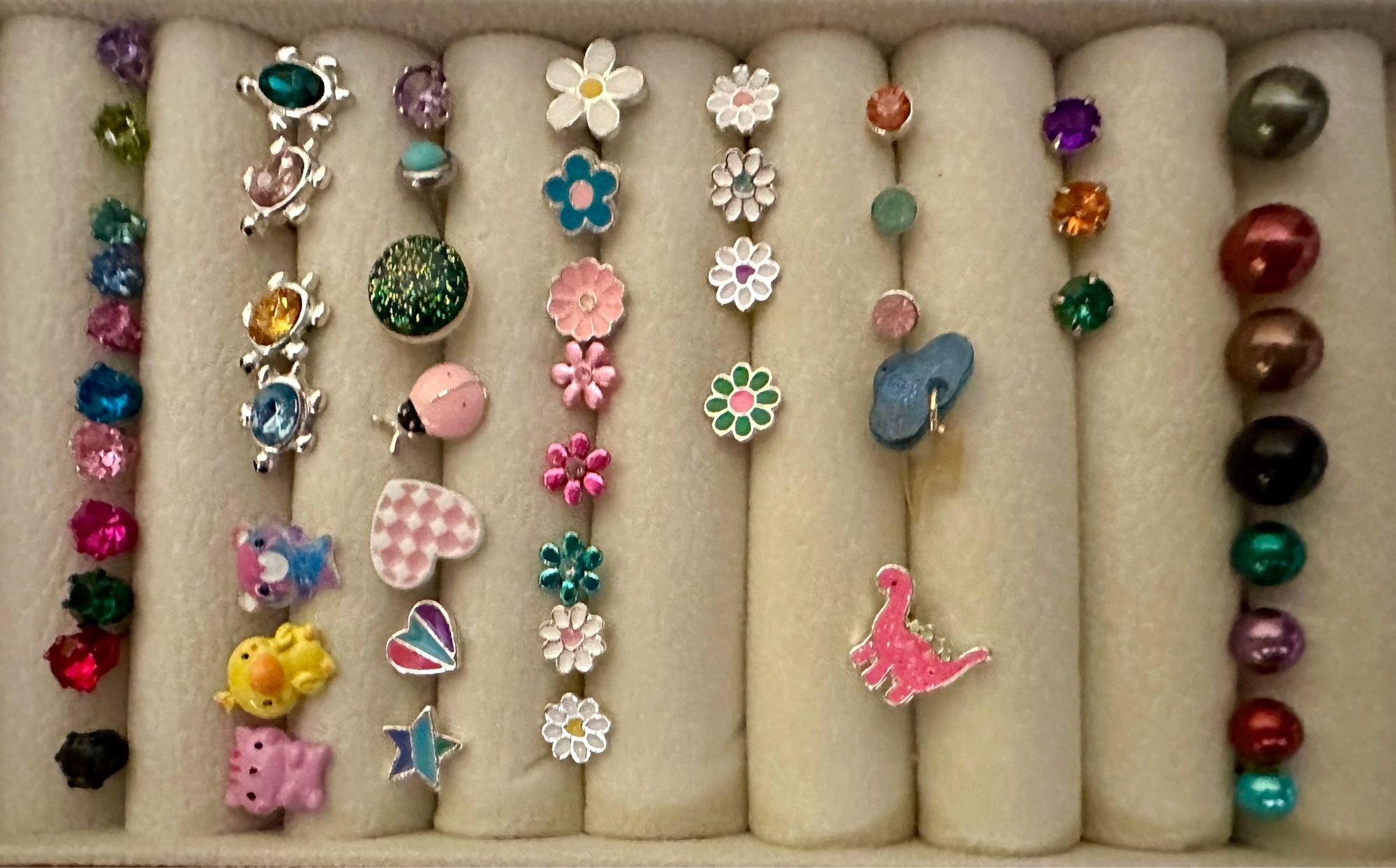 A whole bunch of stud earrings, including a collection of different colored crystals, some silver turtles with different colored gems in them, a pink cat yellow duck and biflag colored bear some hearts stars a ladybug a collection of flowers in different colors some fake solid colored pearl things a pink dinosaur, and a blue cloud with tiny dangling lightning bolt