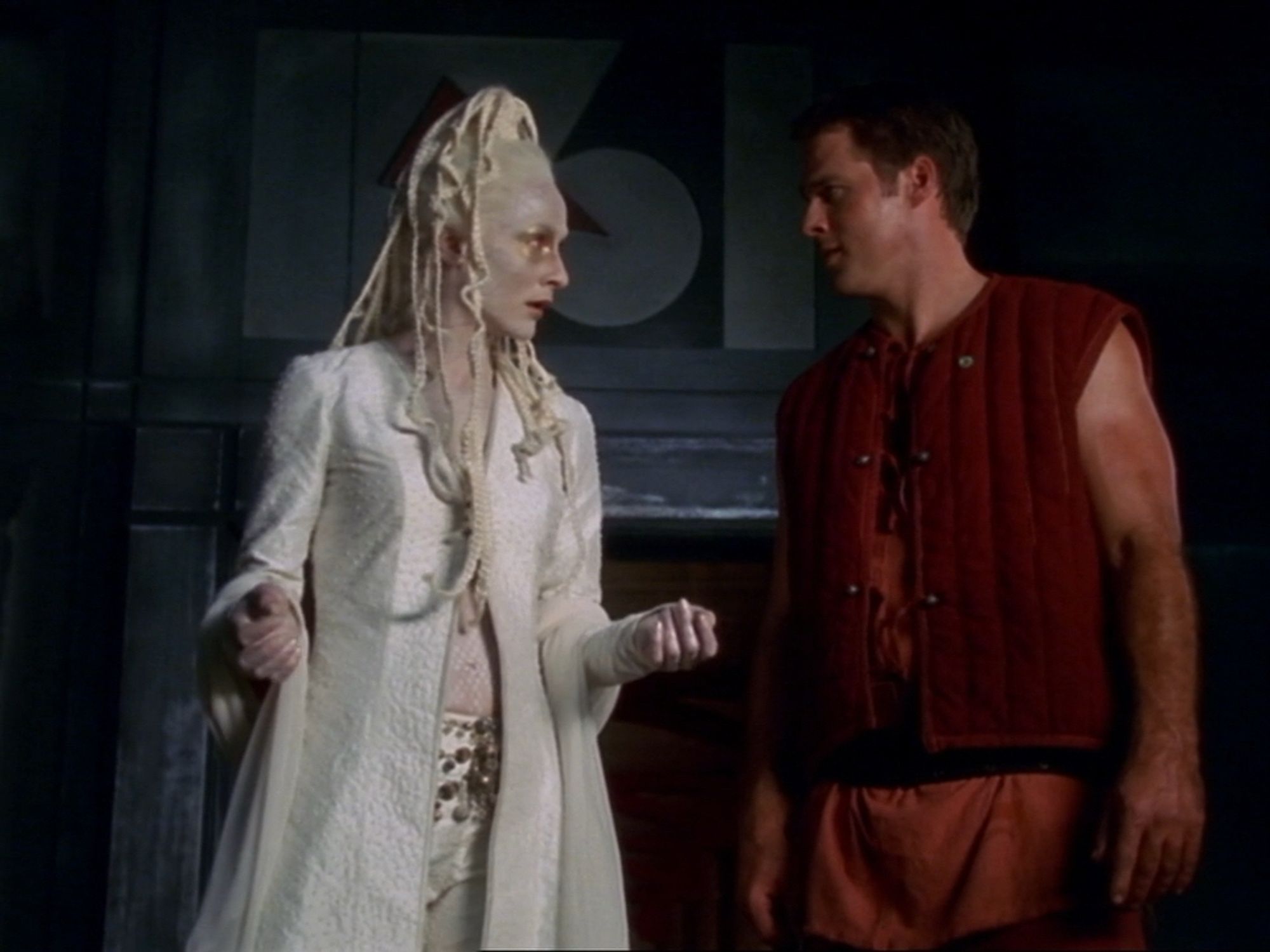 A screenshot from Farscape with an alien woman all in white and John. The plot of the episode is that they are on a planet where the ppl are forced to mine for ammo for weapons but they don’t know that. They are told every day that tomorrow is a rest day but every day they work because they have these parasite so in them that affect their brains and make them agreeable.