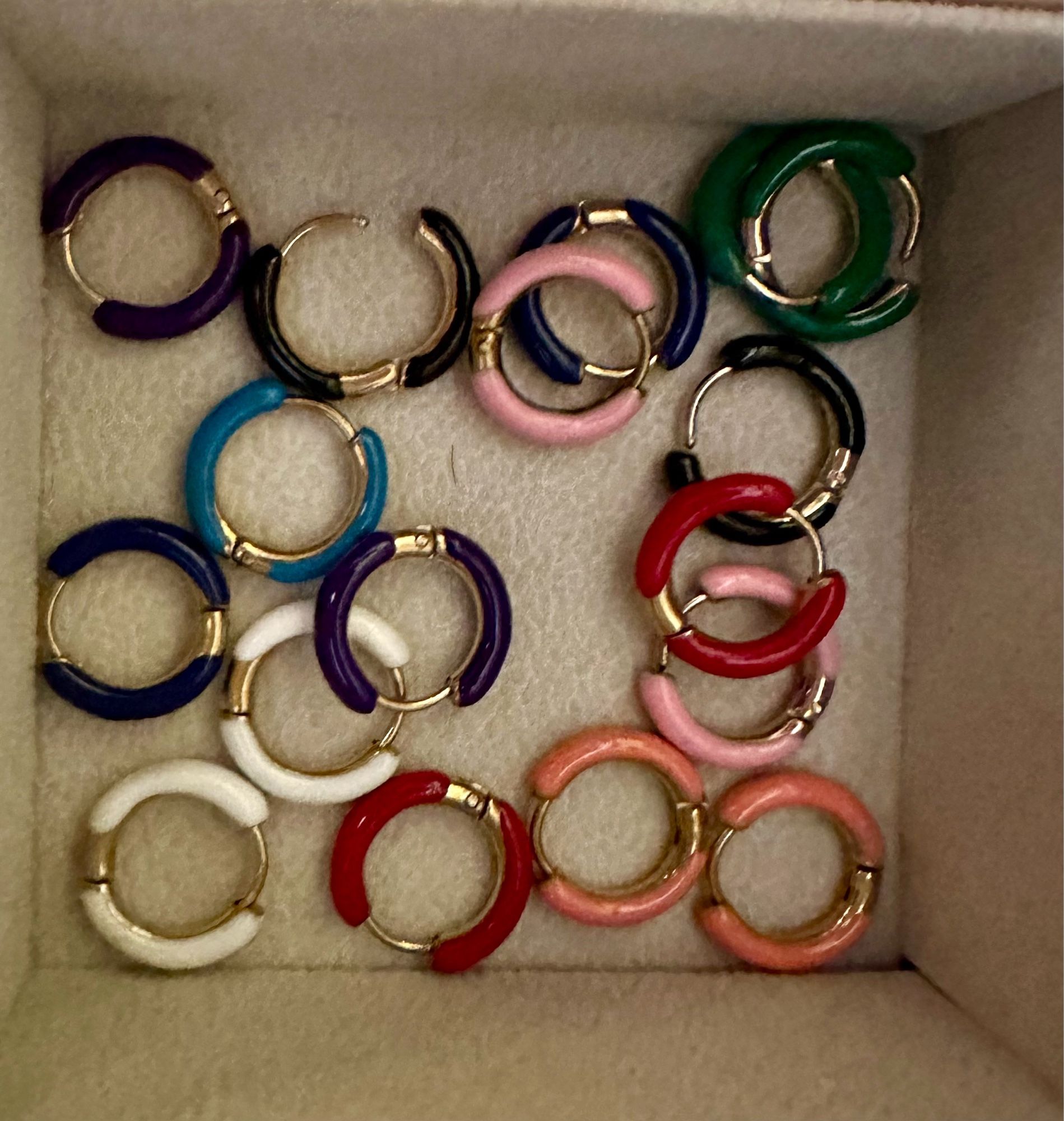 A bunch of gold hinged hoop earrings with color on either side there are some navy and purple and black ones that all seem to appear black in this picture. There was also one light blue one missing because I am currently wearing it.