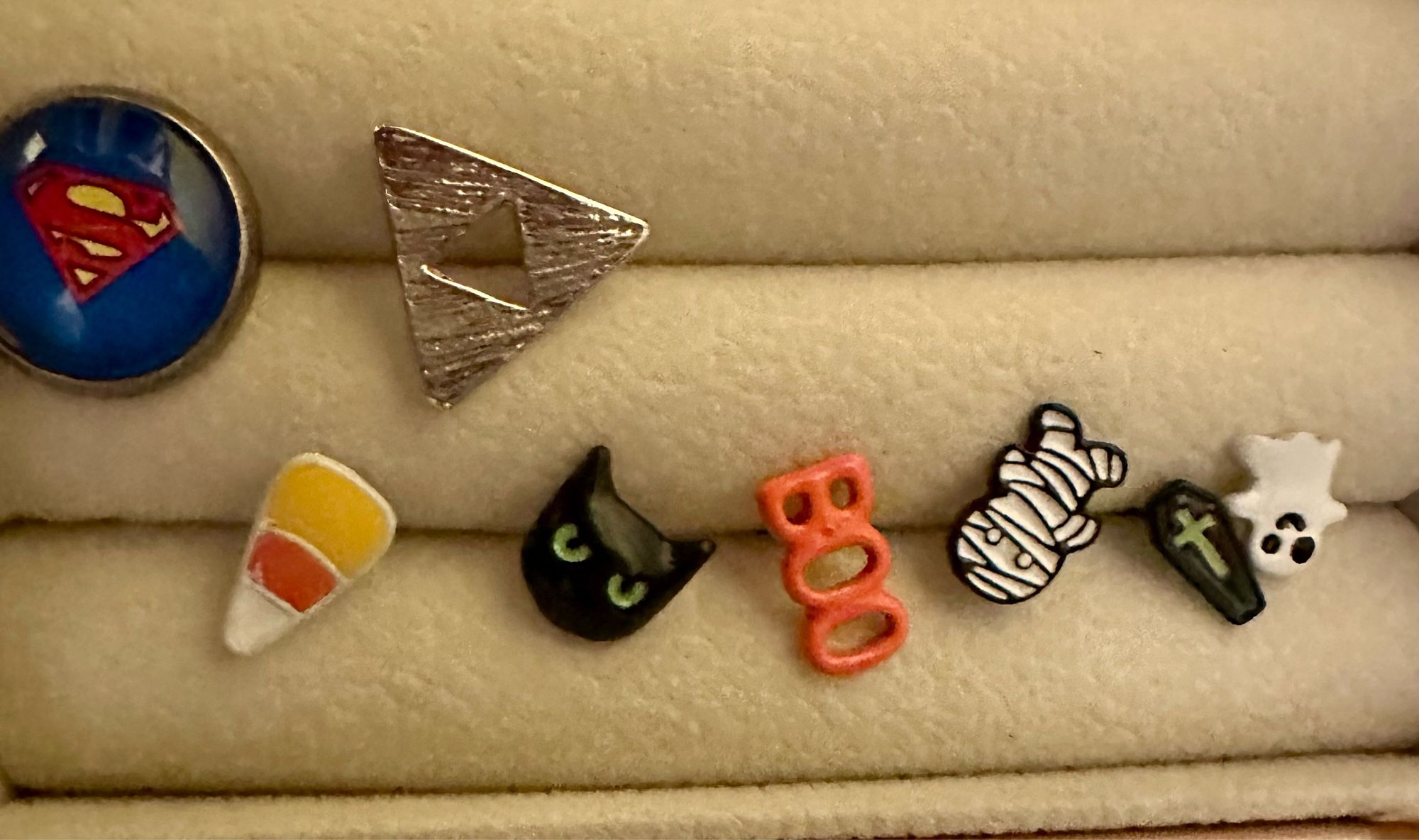 A bunch of Halloween themed earrings including a ghost, a coffin, a mummy, the word, boo, a black cat head, and a piece of candy corn. Also a tri-force and a superman logo.