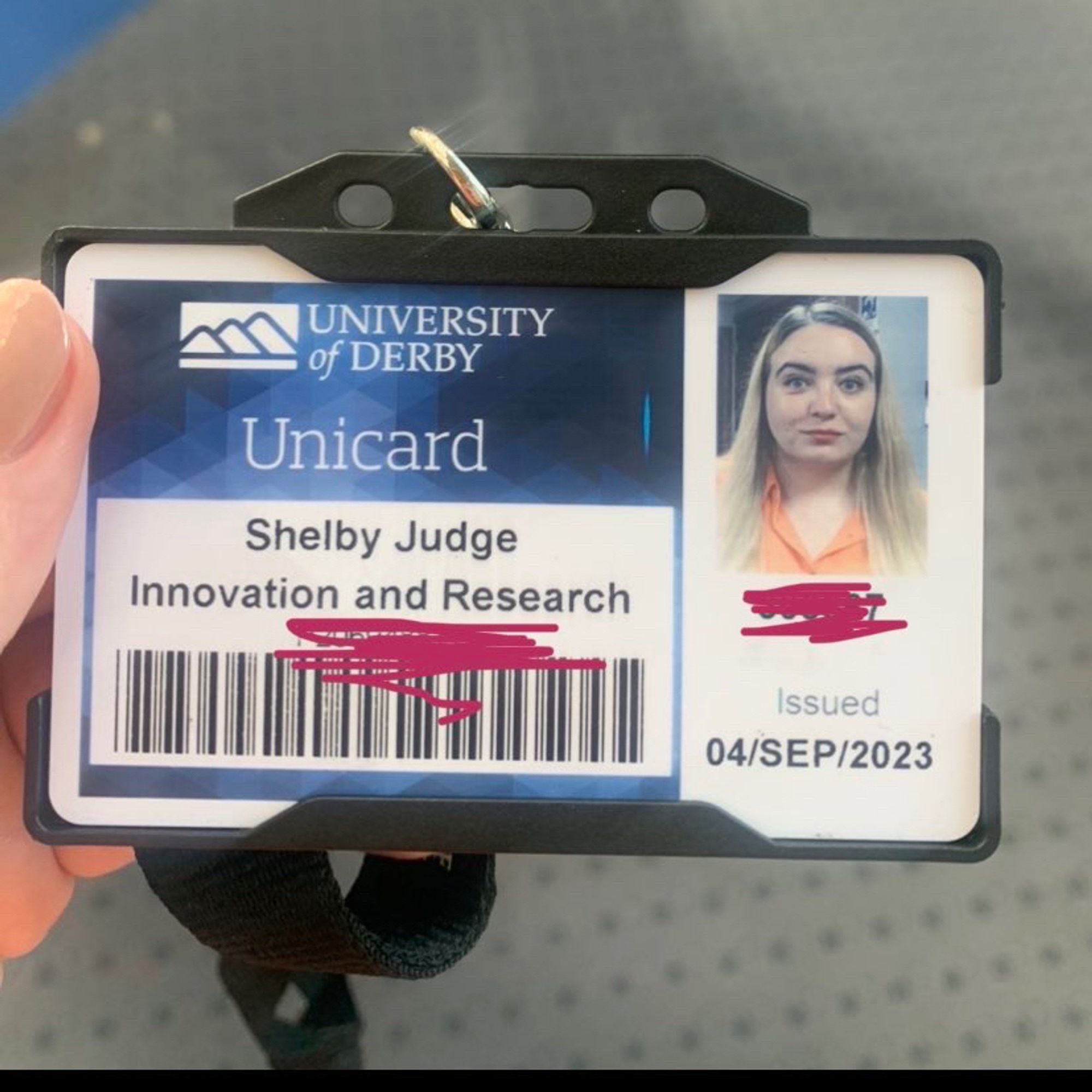 A white hand holding an ID card. The card has a picture of a white woman with blonde hair and the text:
University of Derby unicard
Shelby judge 
Innovation & Research