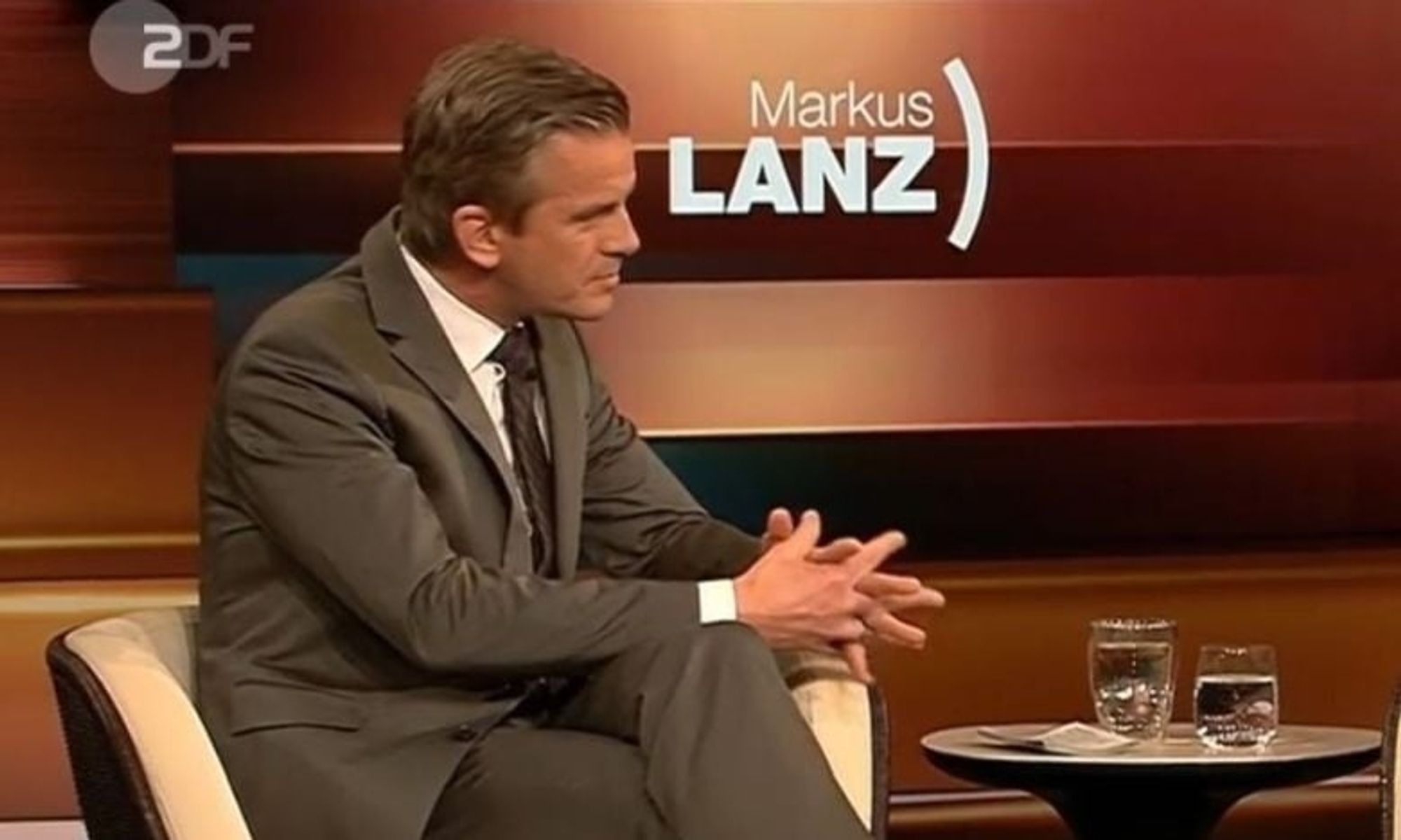 Markus Lanz sitzt im Studio, leicht nach vorne gebeugt.