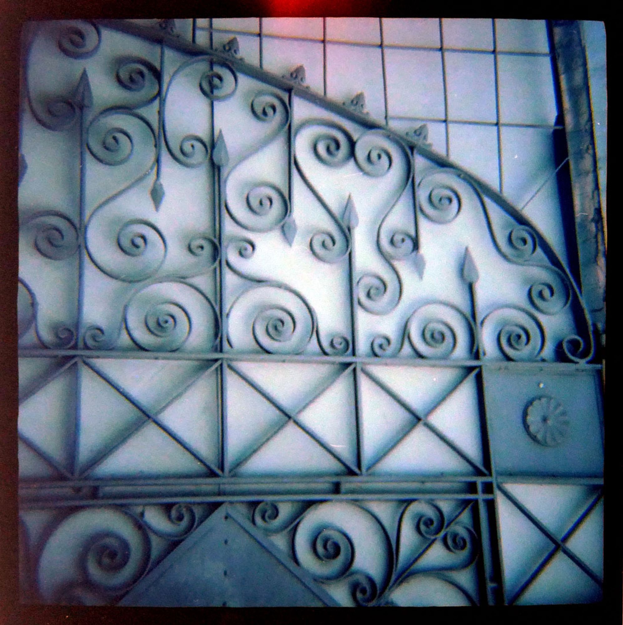 A color photograph showing one section of an elaborate metal gate with spirals, medallions, x-shapes, and arrowheads.