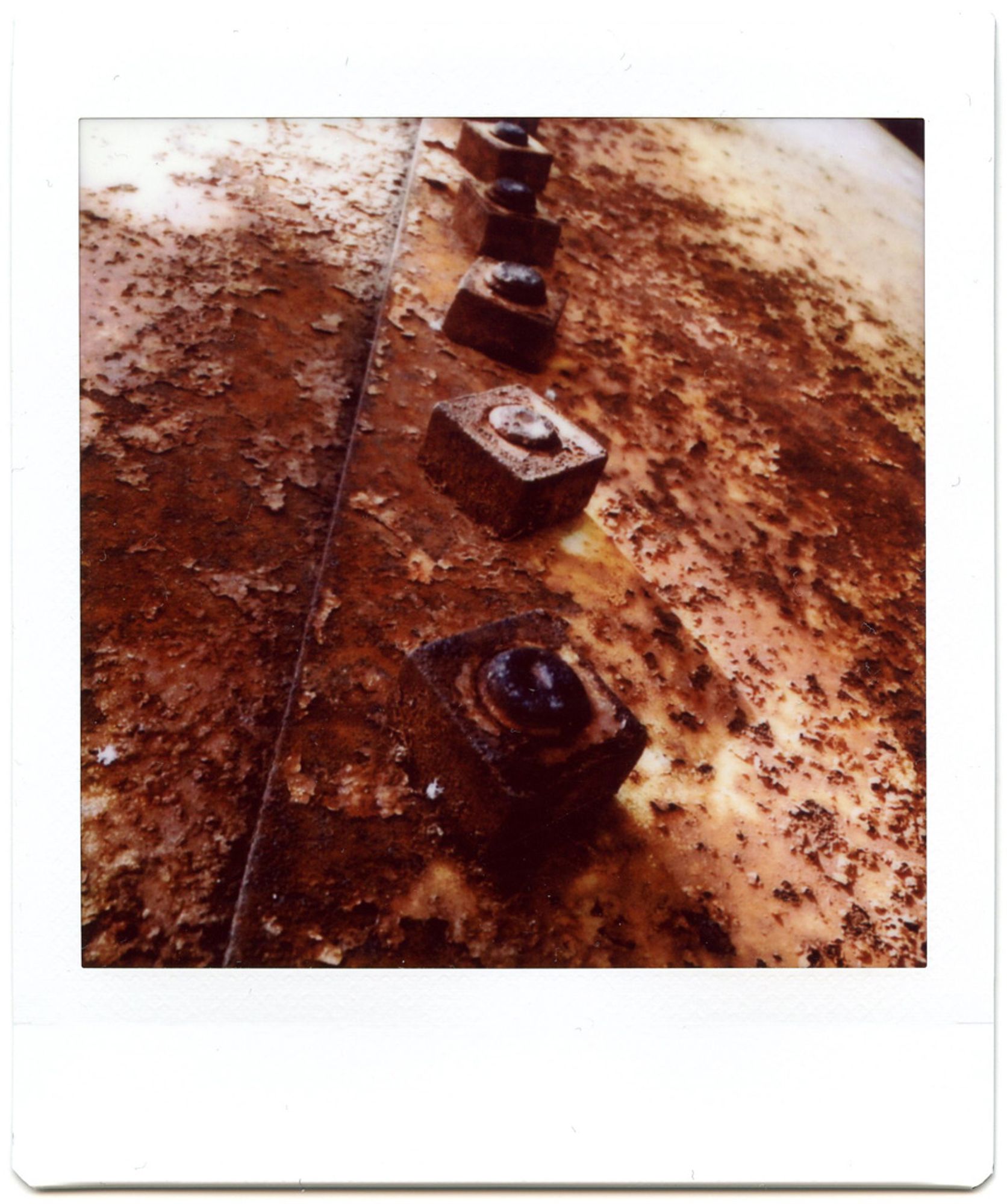 A color instant photograph of five rusted nuts spaced diagonally on the vertical seam of an old, rusted silo.