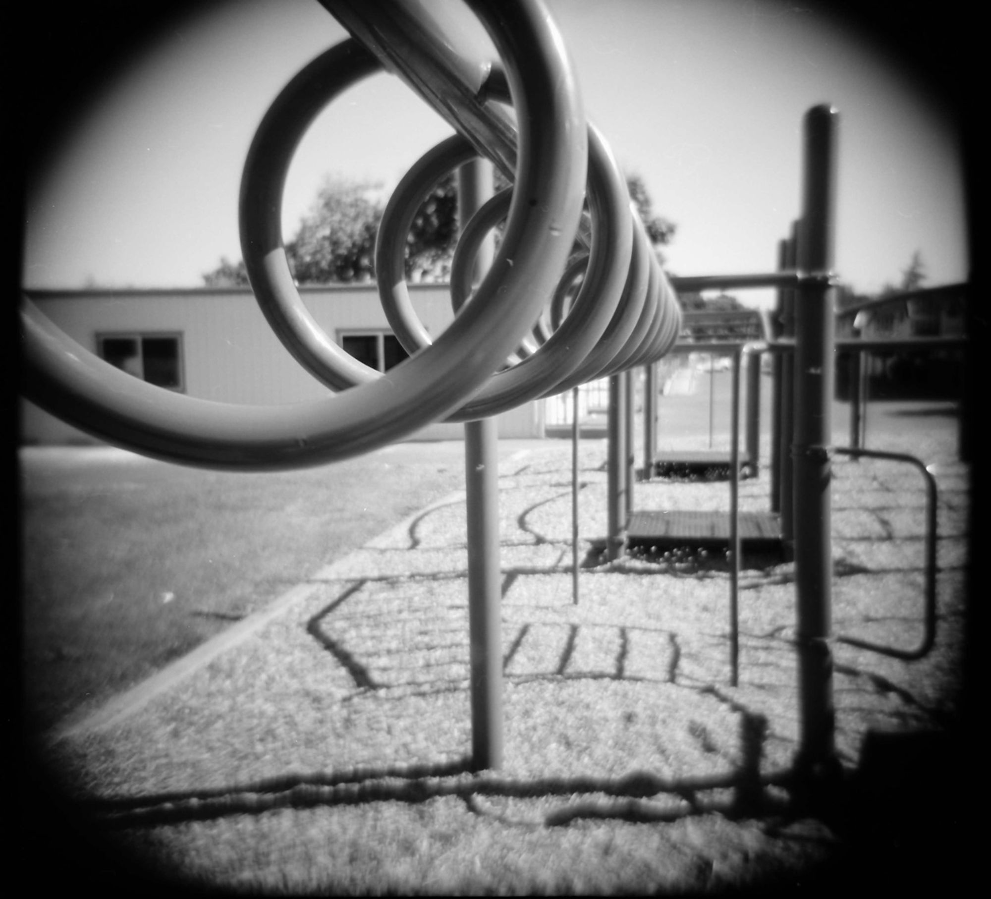 A close-up black and white photograph looking through the rings in an elementary school's set of playground equipment.