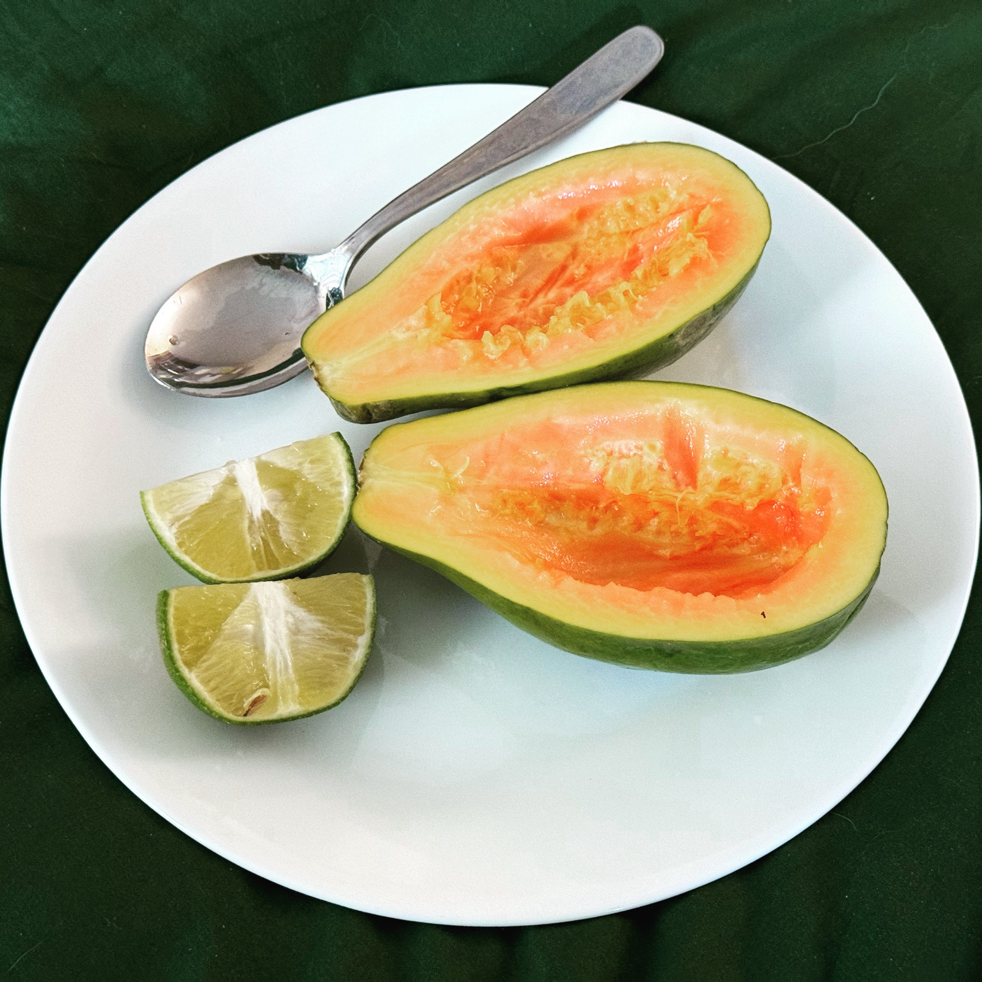 A brightly colored fresh local papaya, halved and seeded, on a plate with two lemon slices.