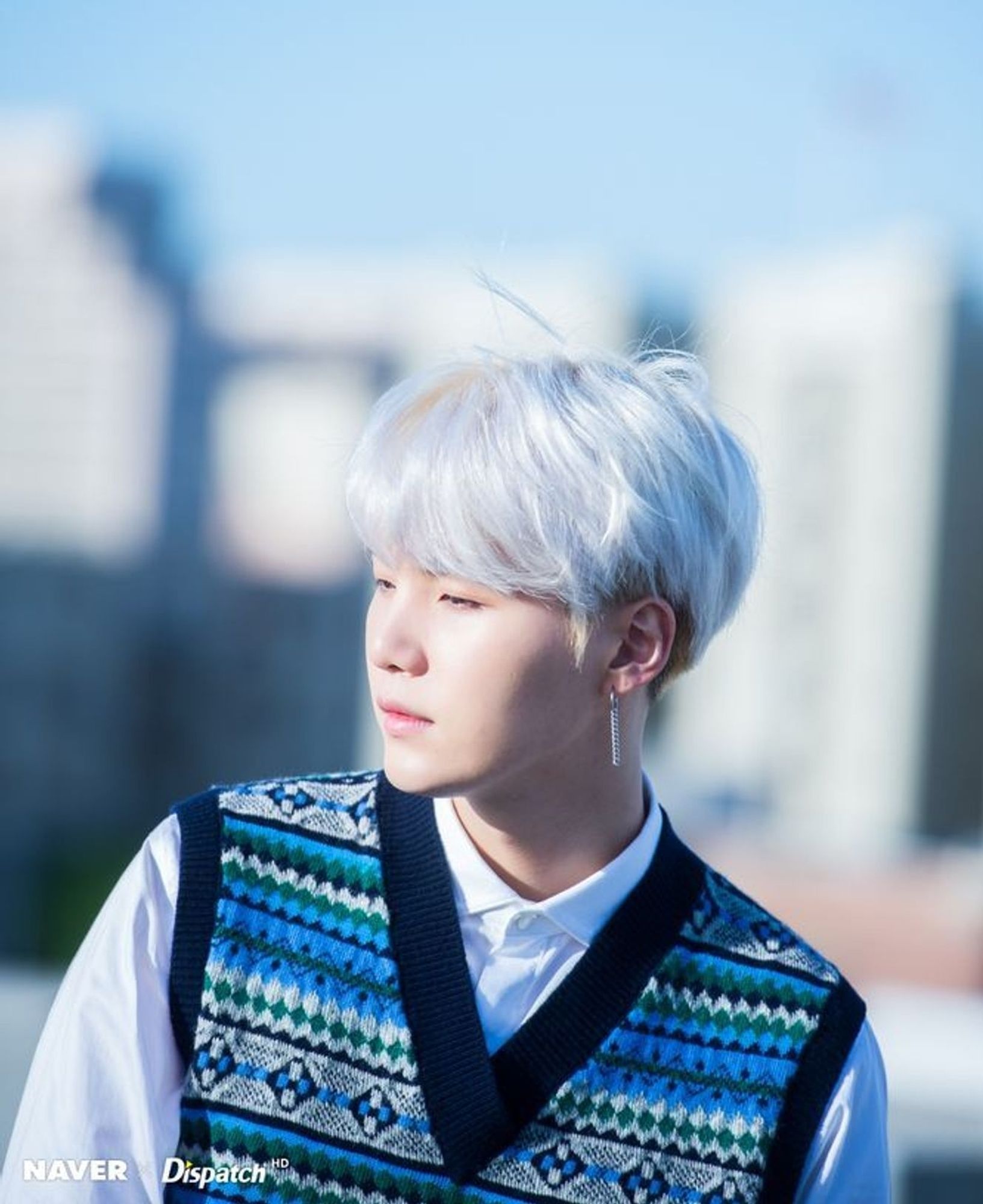 Min Yoongi with white hair, he's wearing a long sleeved shirt and a blue colored vest.