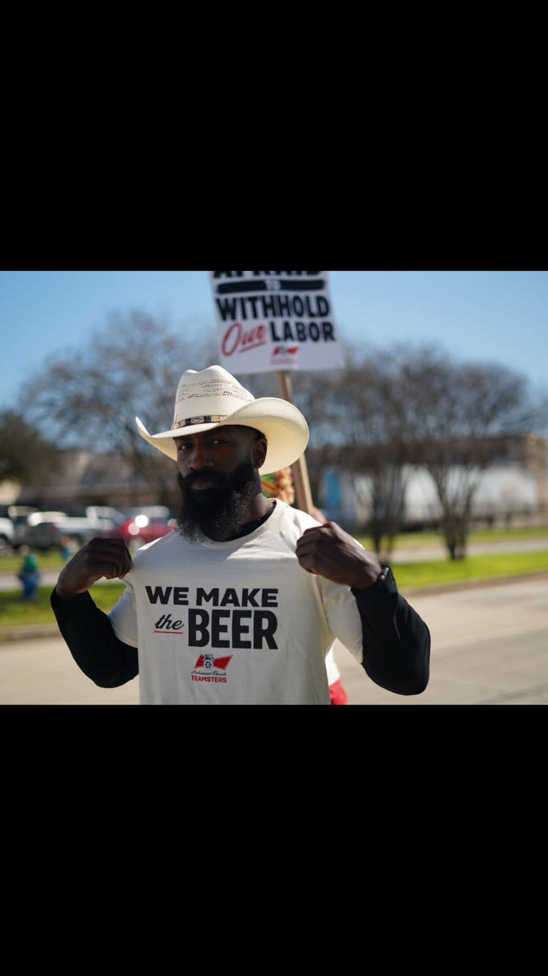 Picture of a Black man in a cowboy hat wearing a shirt saying we make the beer and it goes hard as hell