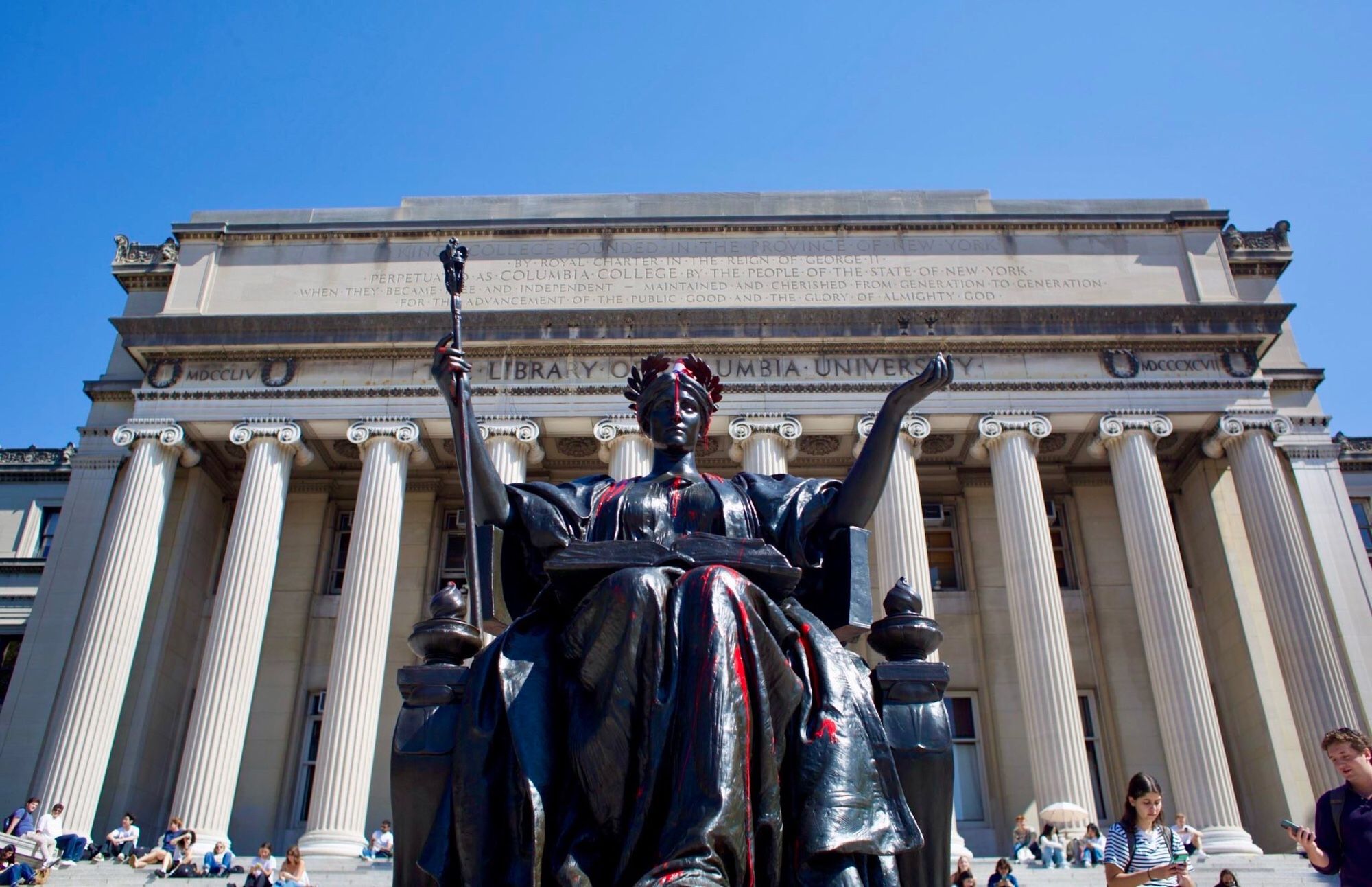 Photo of the statue in red paint from the front with Columbia university in the back