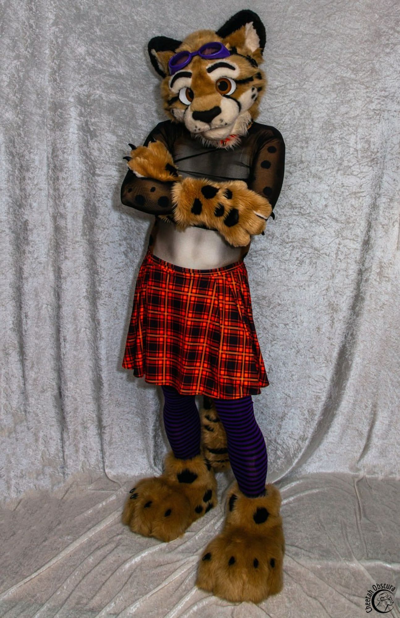 Obscura in fursuit partial and spandex bodysuit, dressed in a sheer croptop, orange plaid skirt, and purple/black stockings standing in a confident sassy pose