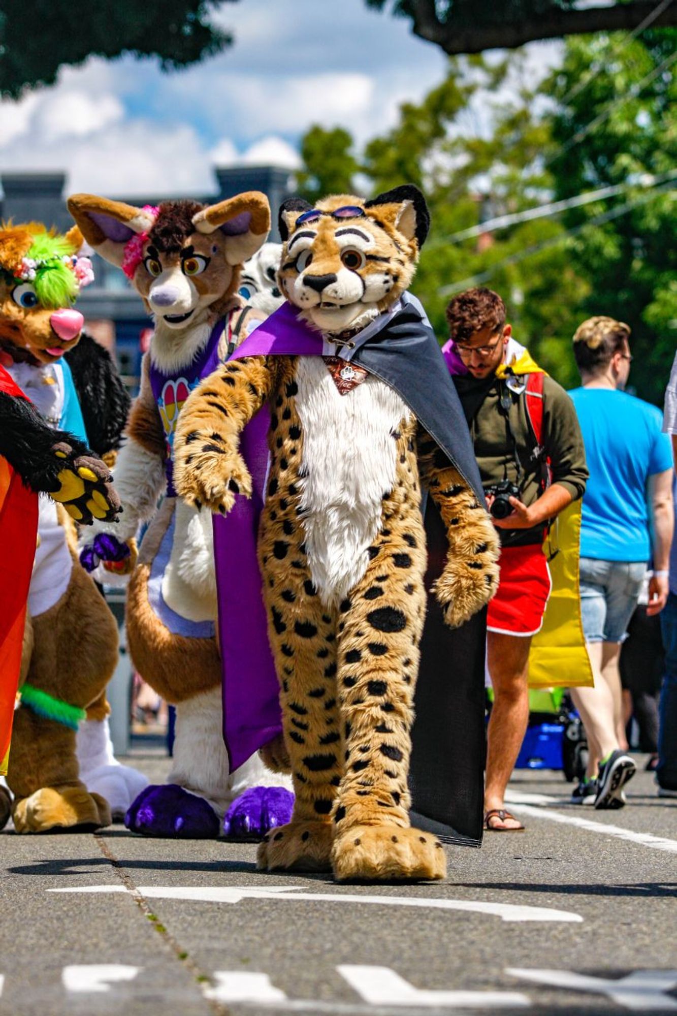 Obscura walking confidently towards the camera at a Pride celebration with an asexual flag worn as a cape