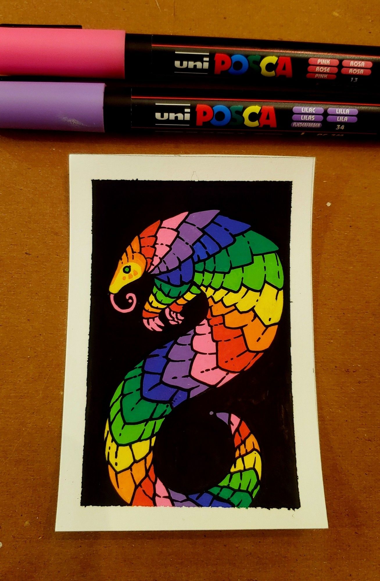 Photo of a small acrylic paint marker painting of a rainbow pangolin.