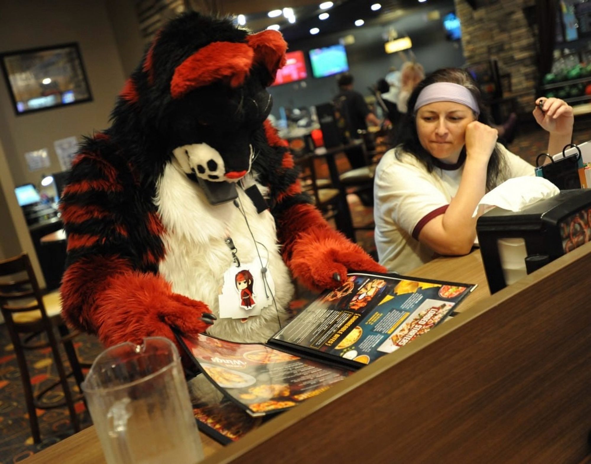 A person in fursuit reviewing a menu while another person looks on.