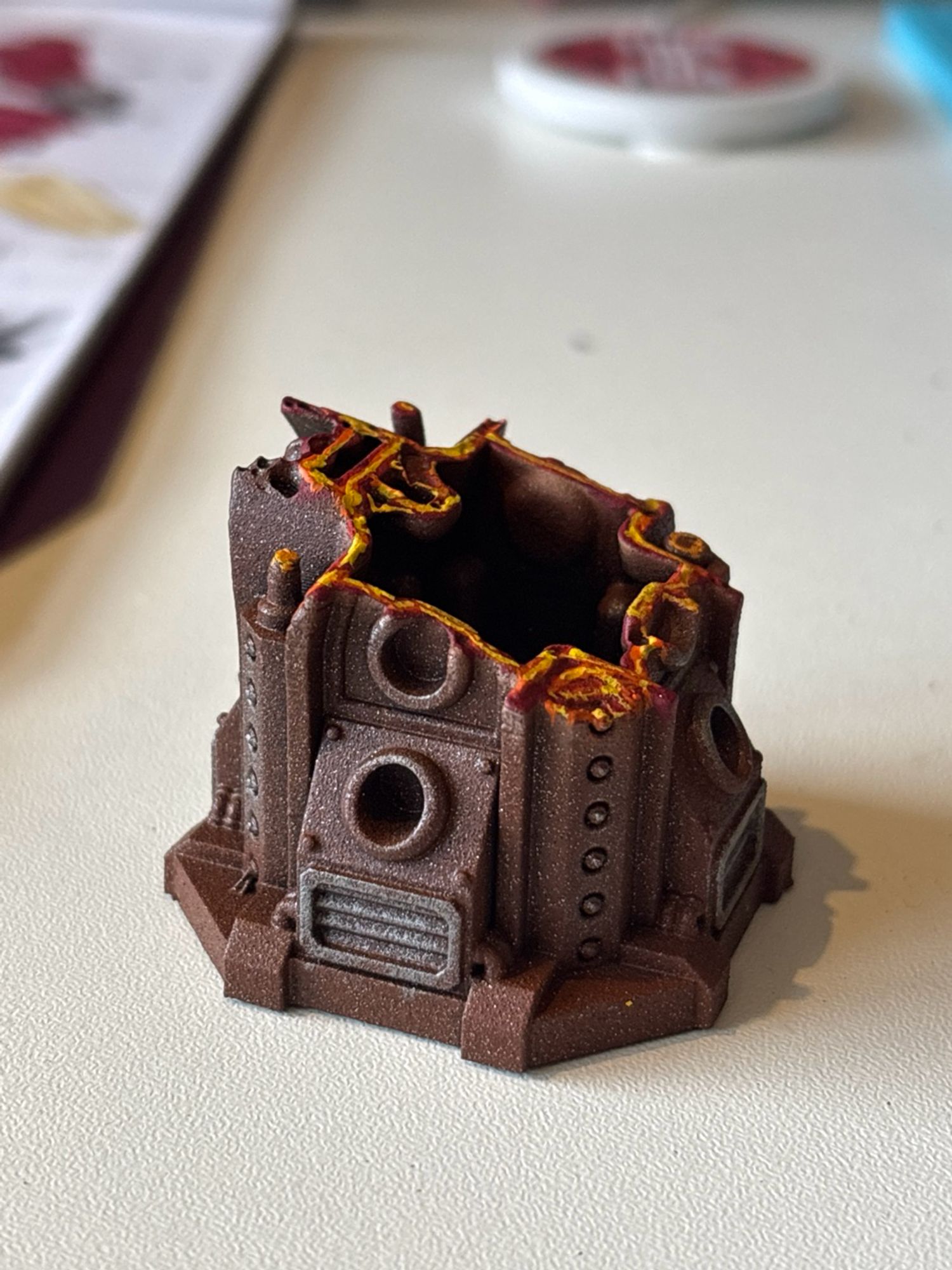 A small model of a piece of rusty grimdark scenery with a diagonal slice across it which has removed the top half. The slice is painted to look like molten metal.