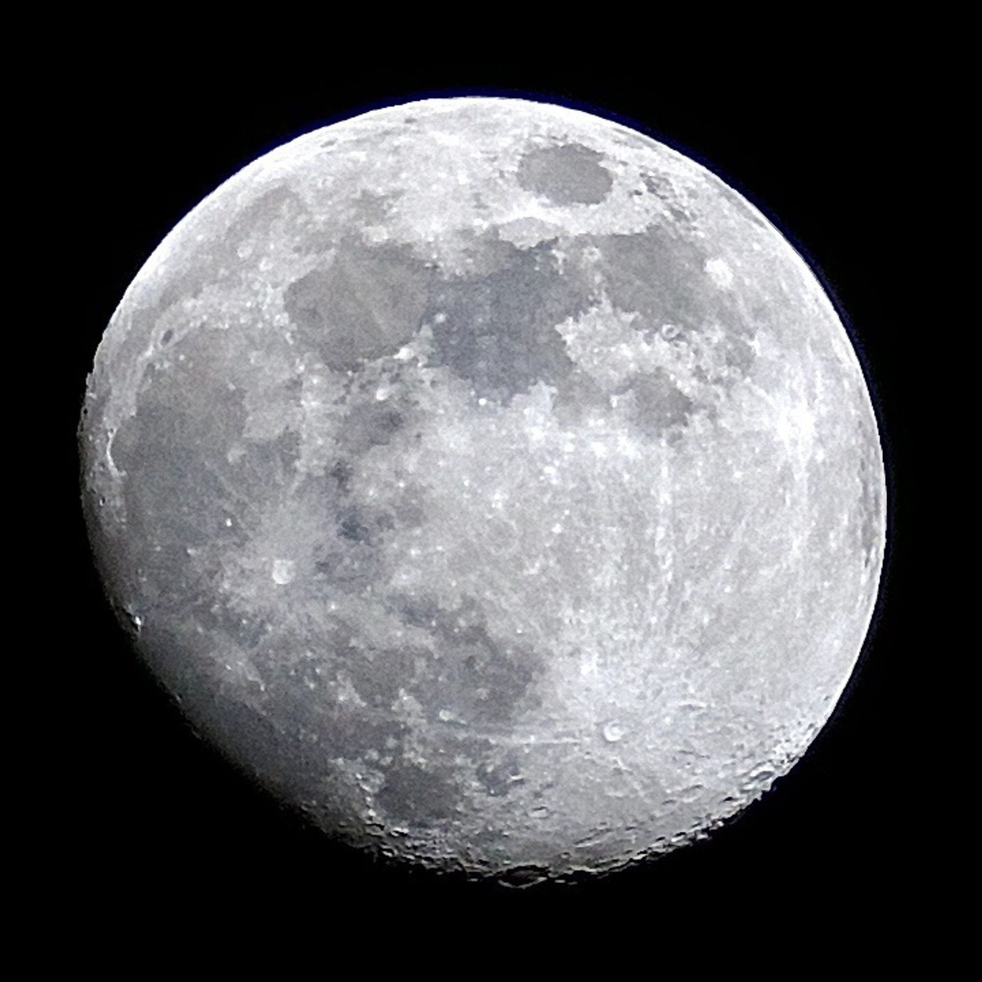 An almost full moon on a dark background.  There are impact craters of various different sizes and dark grey regions which were once seas of volcanic lava.