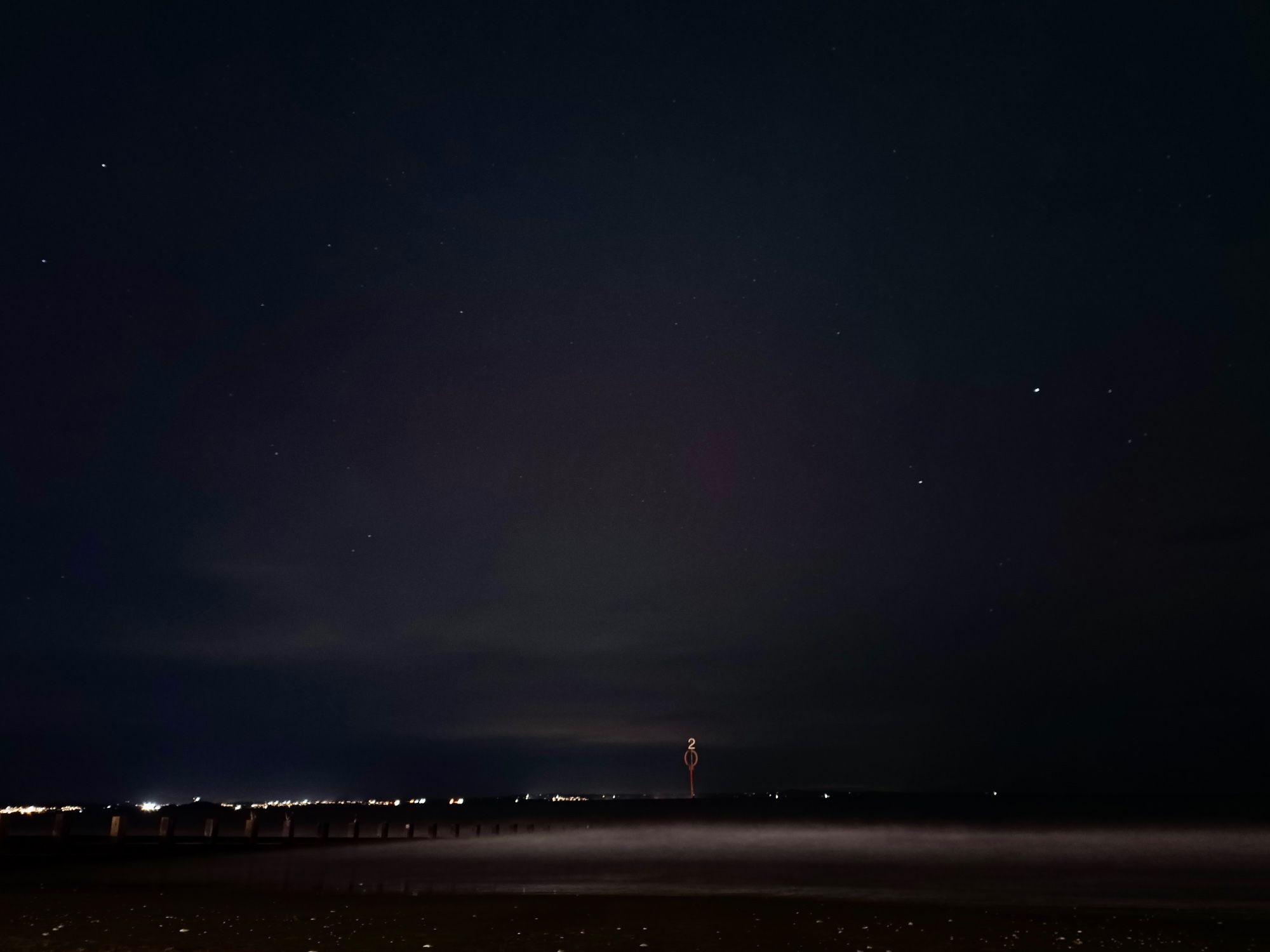 A beach at night time.  There is a pink glow in the sky.  Some stars dot the background