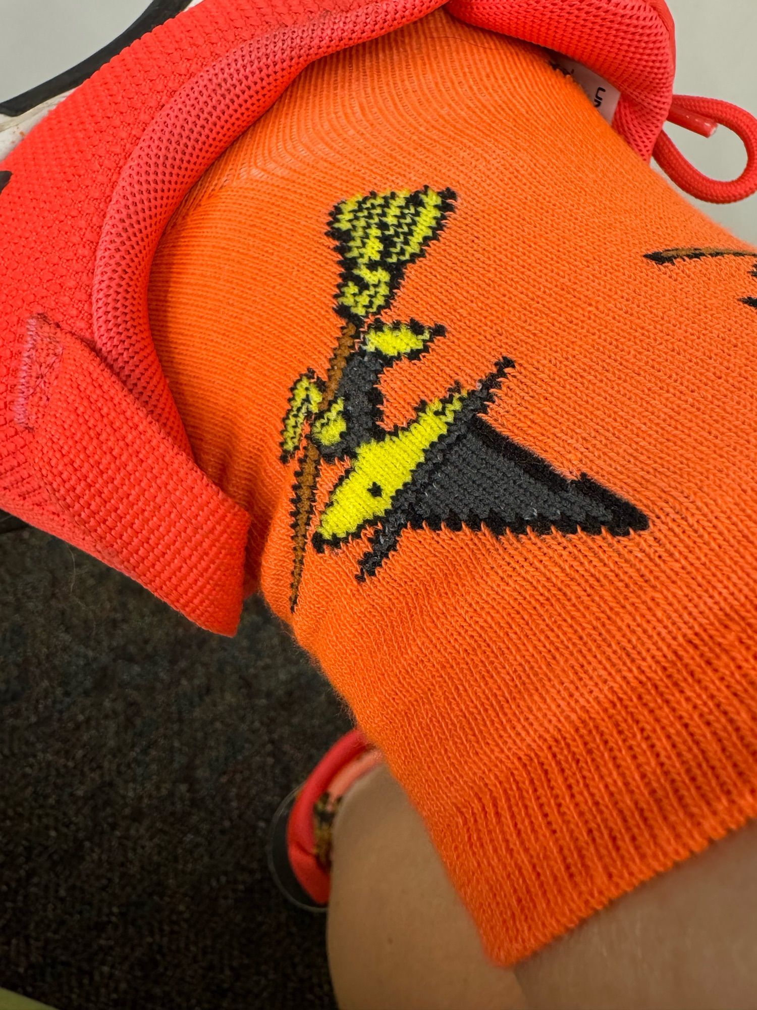 A close-up of my ankle. I am wearing Halloween orange socks with a large Woodstock (of Peanuts fame), dressed as a witch with a big, black, pointy hat. He is also riding a broomstick and wearing a little black outfit. This level of cuteness should be illegal.