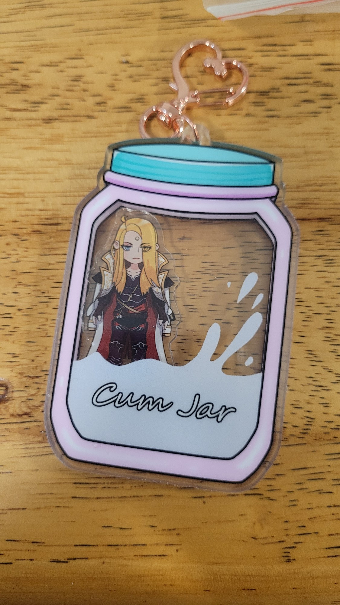 Description: an acrylic shaker keychain charm in the shape of a jar with a smaller charm of the character Zenos yae Galvus from the video-game Final Fantasy 14 inside of it. The jar has the words "cum jar" on it with a white splash inside. 