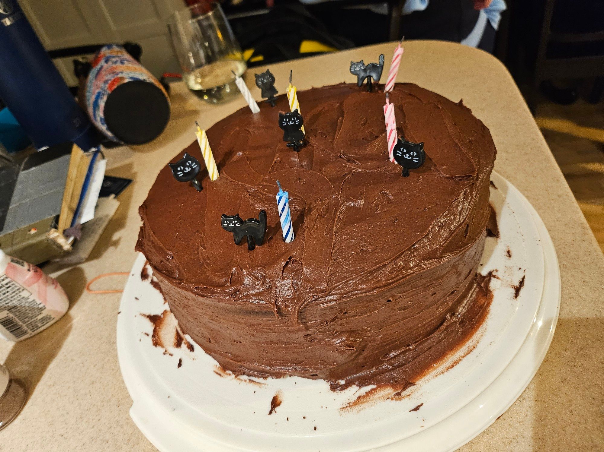 a round layer cake with chocolate frosting sort of smeared all over, with a handful of candles and little black cat toothpicks