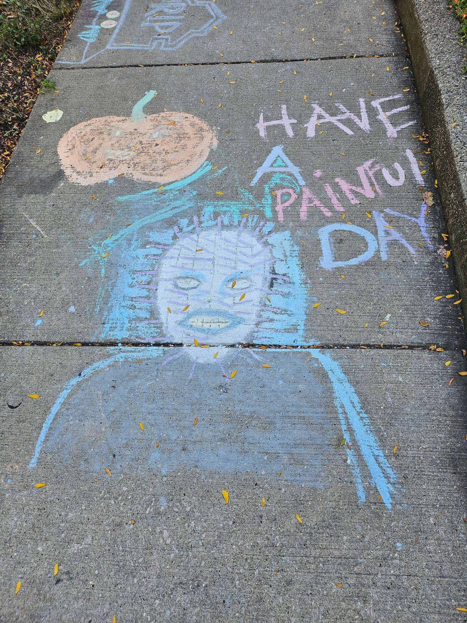 cheerful pastel sidewalk chalk says HAVE A PAINFUL  DAY, near a pumpkin and  pinhead