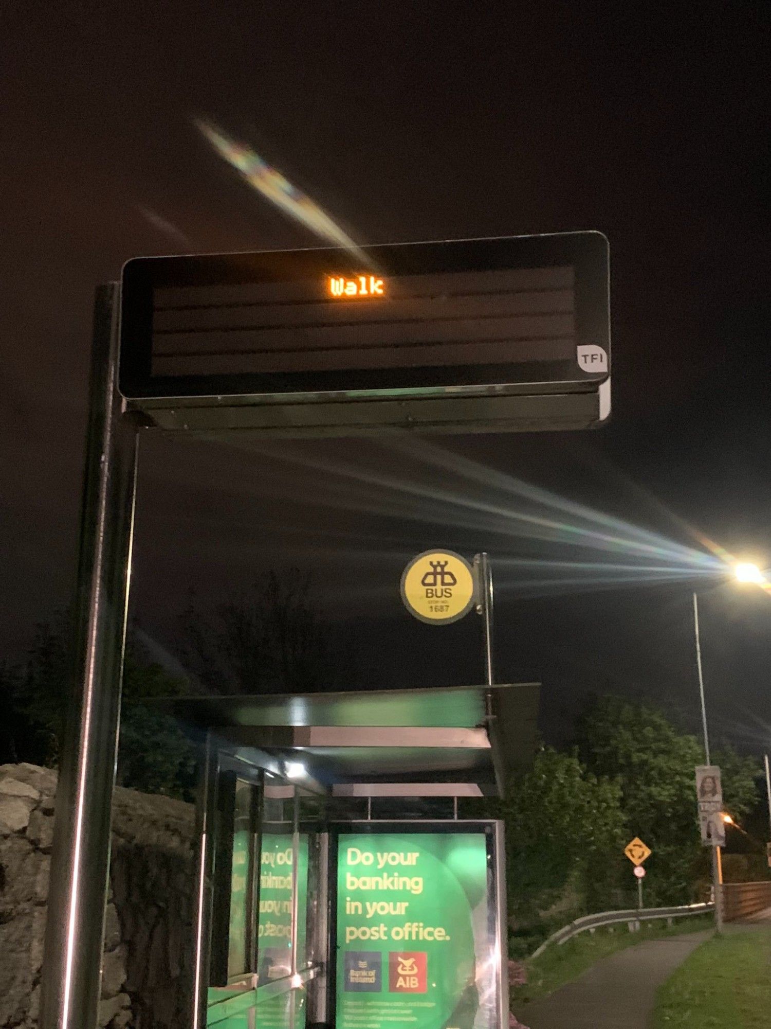 Digital sign over a darkened bus stop that says only WALK