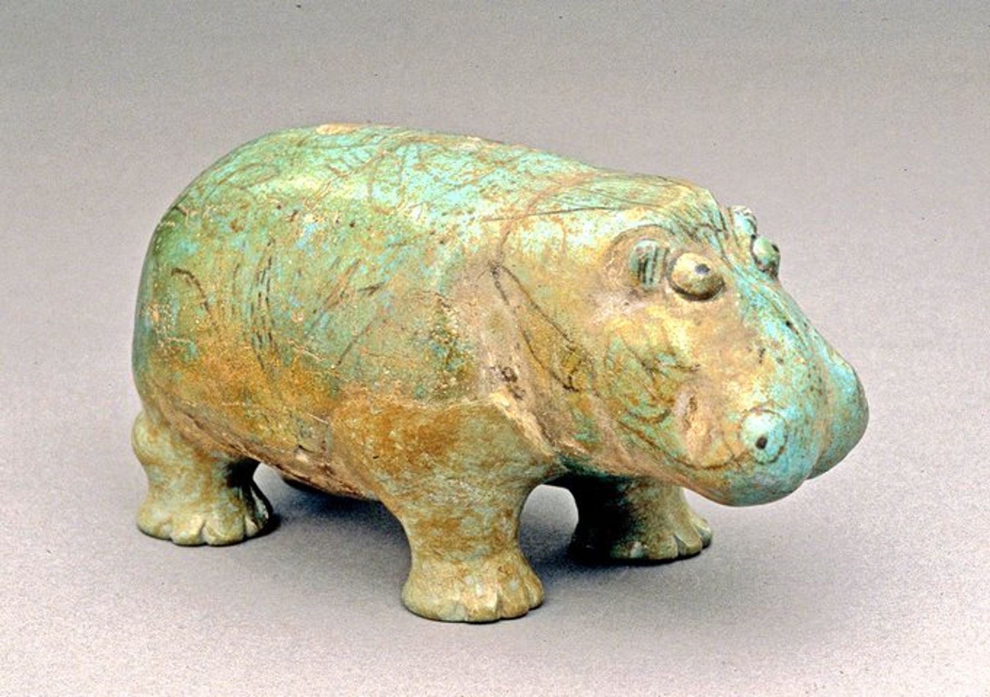 Small ceramic hippo. It is pale green and golden yellow, with tracings of lotus flowers for decoration