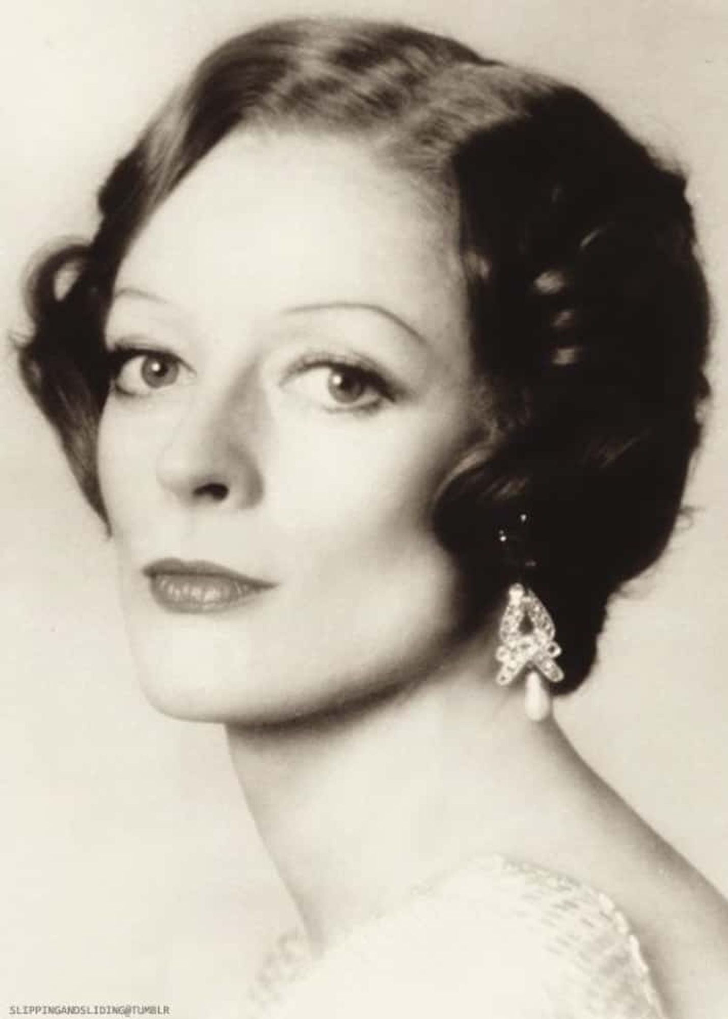 Young Maggie Smith with her hair up, dressed formally, looking both bemused and serious, somehow