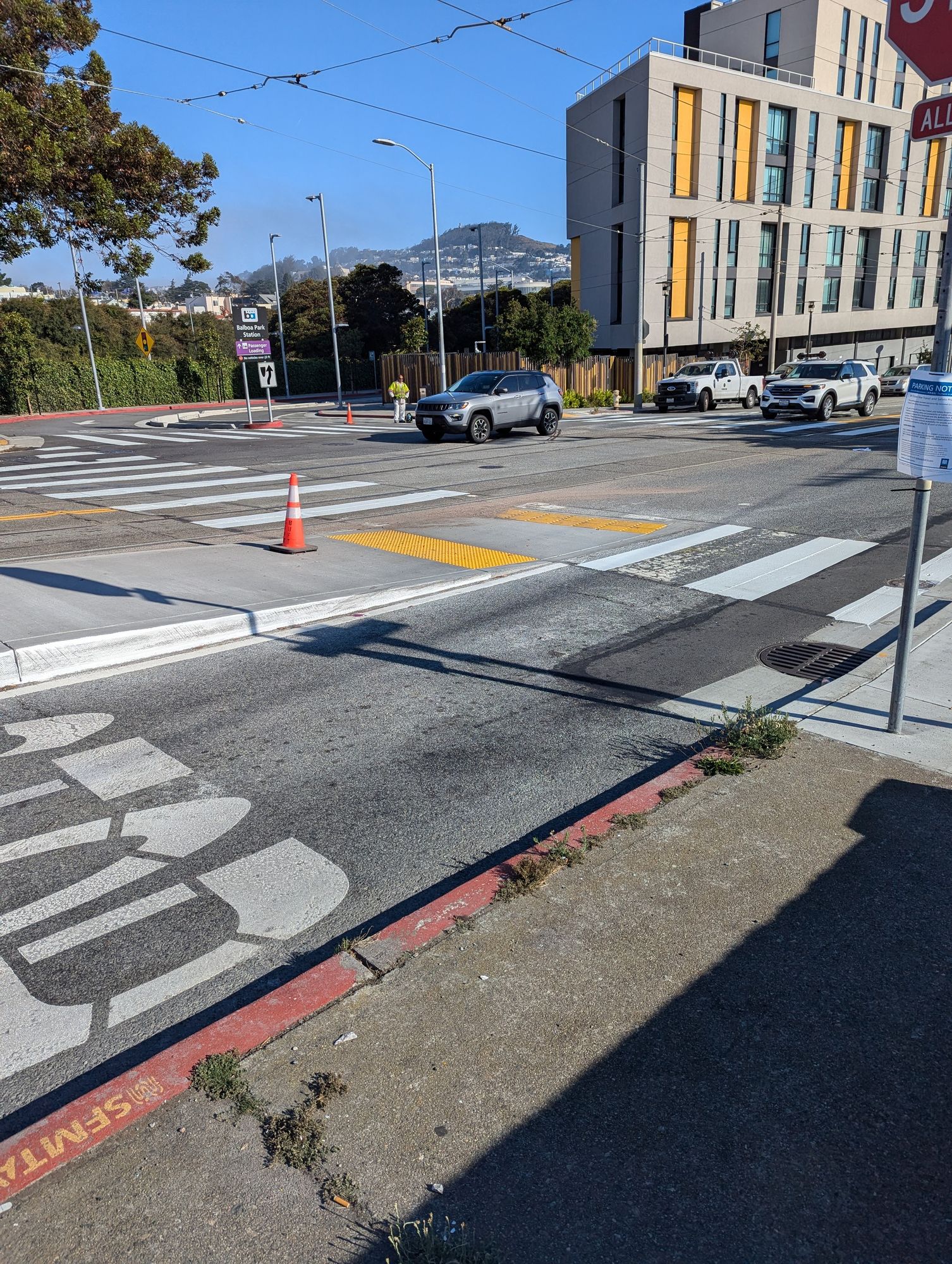 An intersection with freshly marked crosswalks. At the left of the image is a low floor light rail boarding platform.