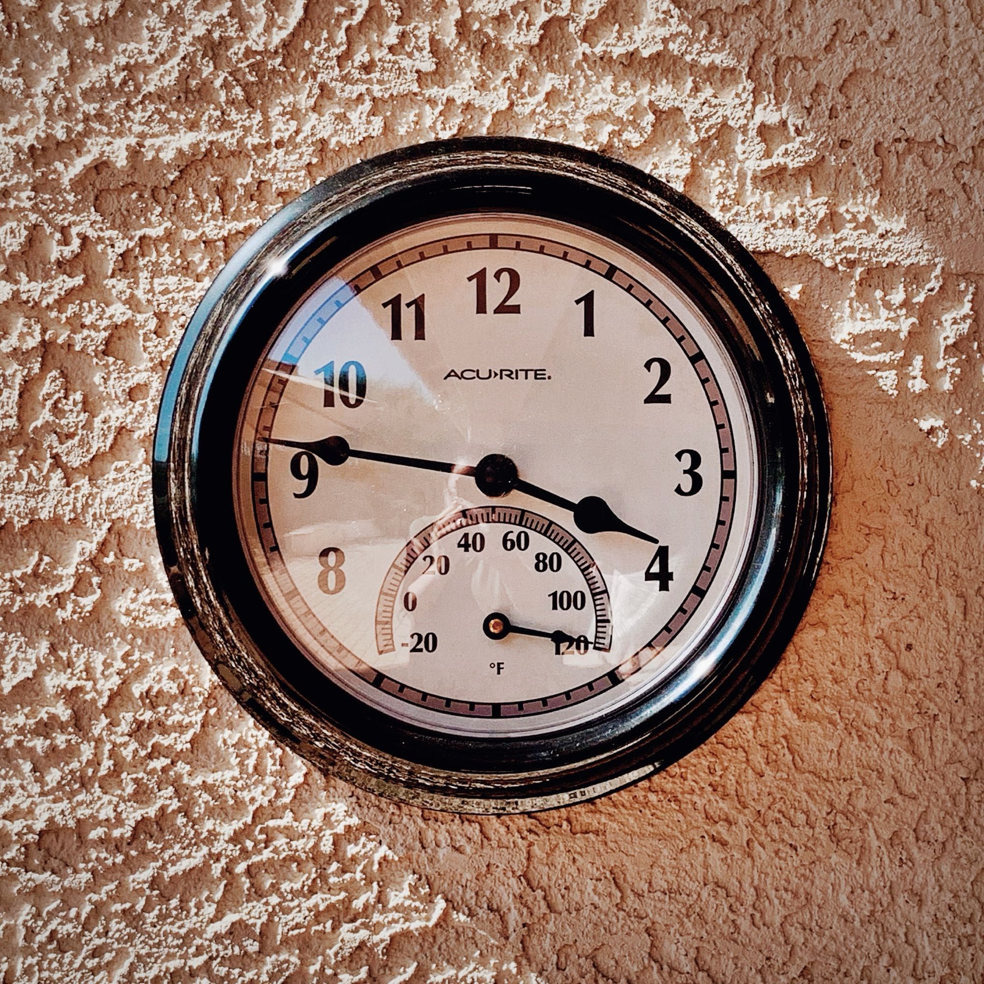 An outdoor clock on a stucco wall, time shows as 3:47, temperature shows as 120F (as high as the thermometer will go).