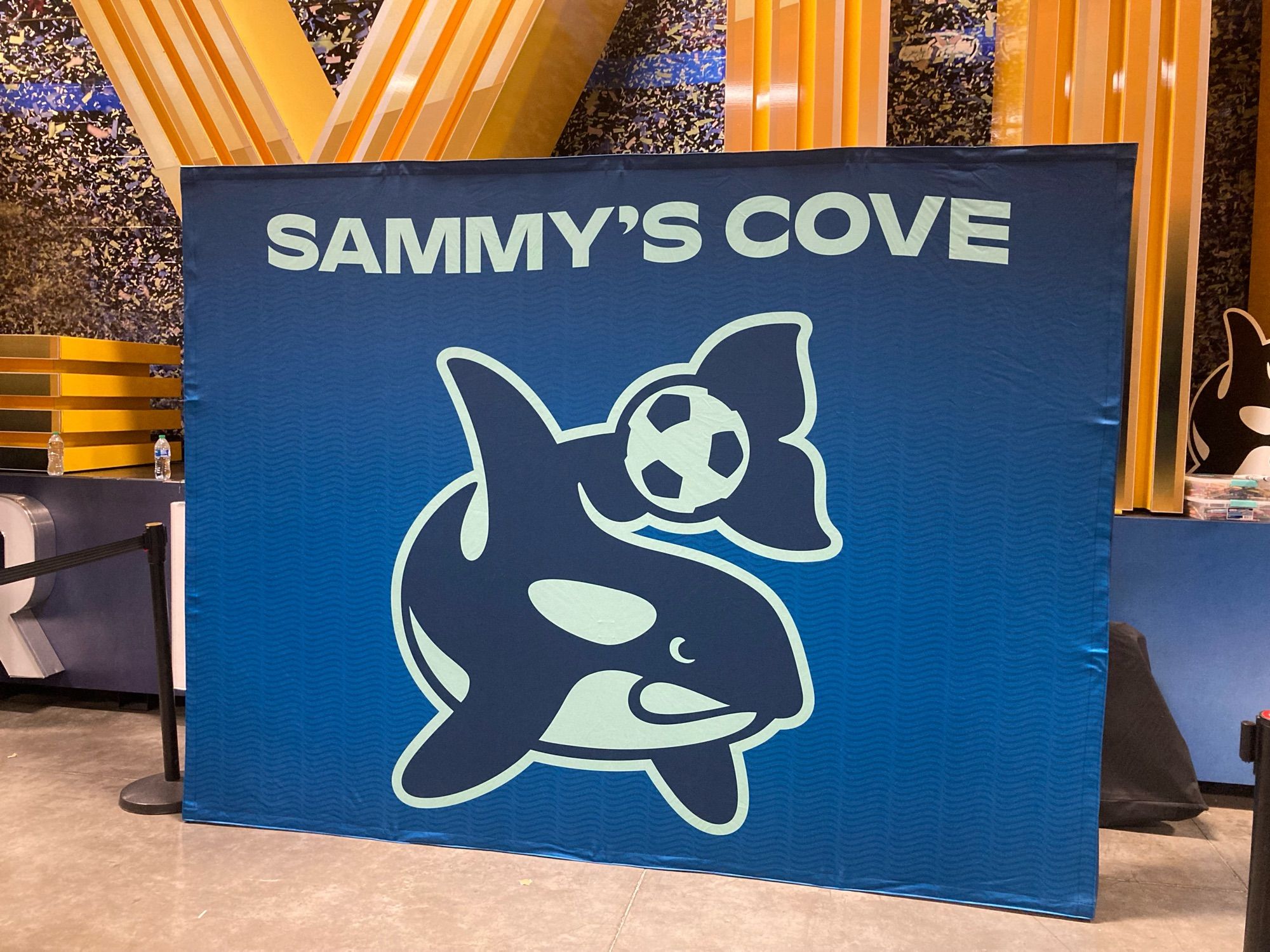 A large banner with a blue background and a giant Orca flipping a soccer ball. Across the top it says ‘Sammy’s Cove’. Go Sounders!!