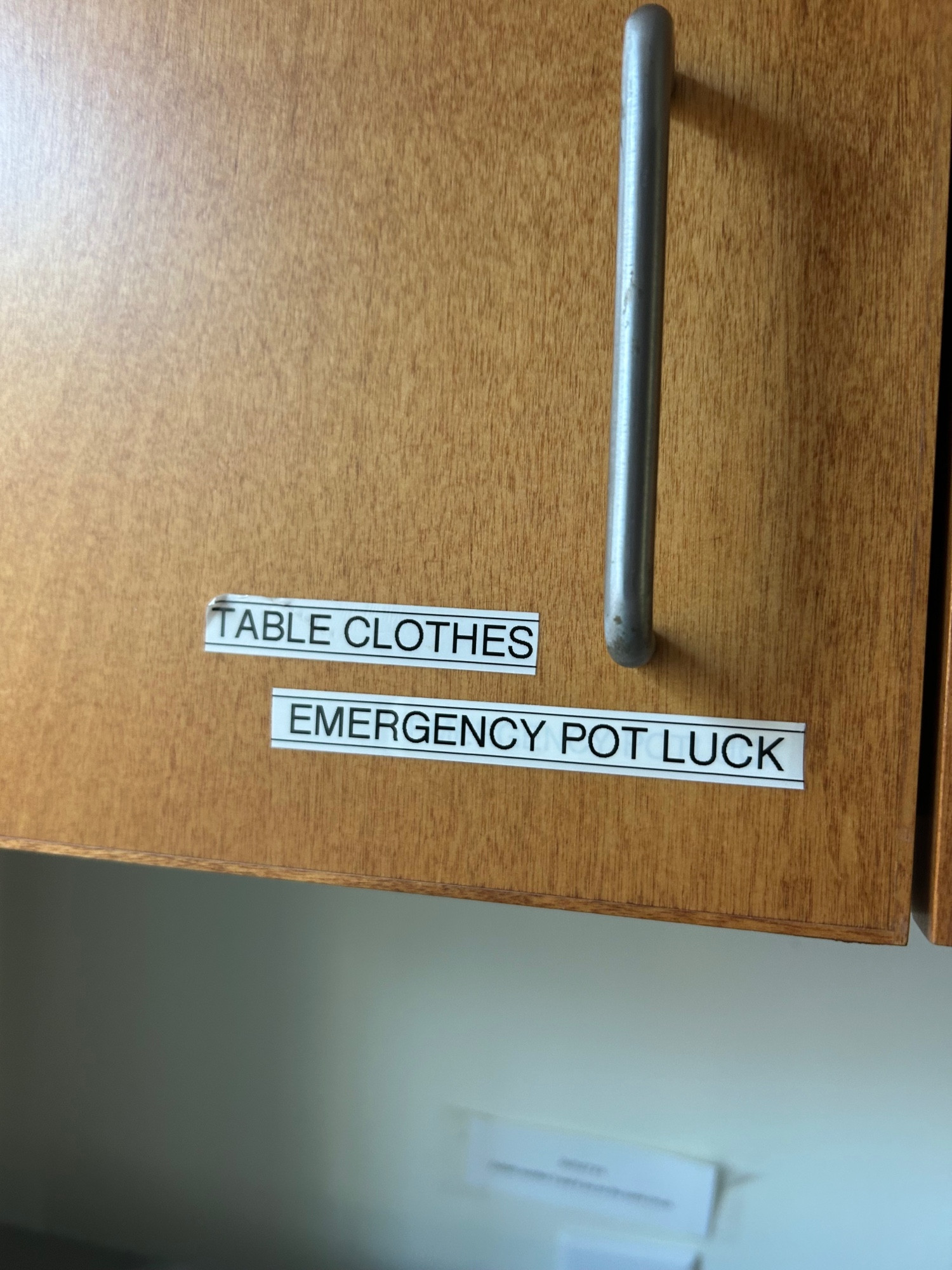 Light brown kitchen cabinet with a label that reads “Tableclothes Emergency Pot Luck”