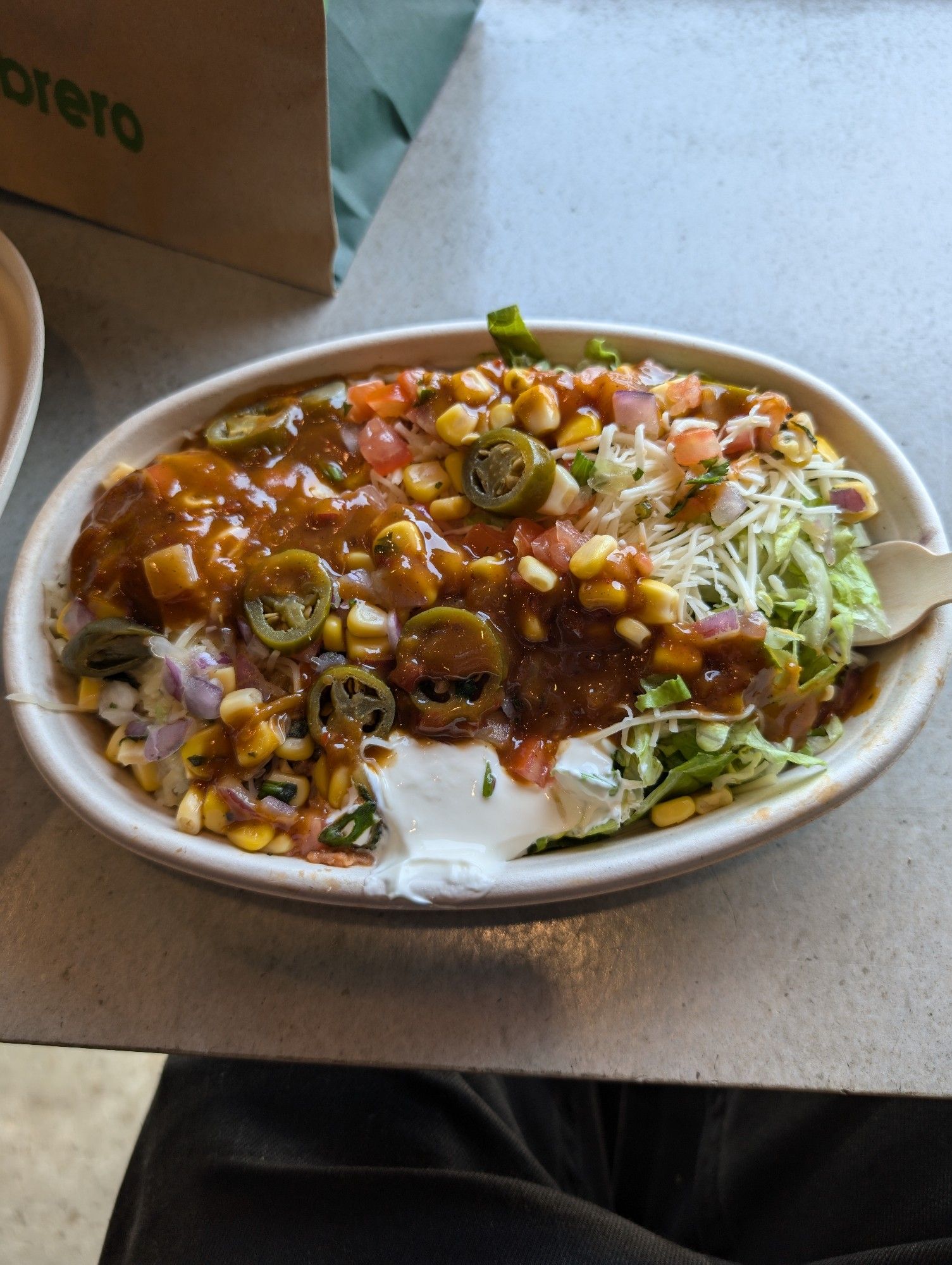 A burrito bowl with jalapeños, chilli sauce, corn, sour cream, lettce, meat, and cheese