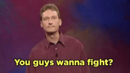 White male standup comedian in red shirt with yellow text overlay "you guys wanna fight?"