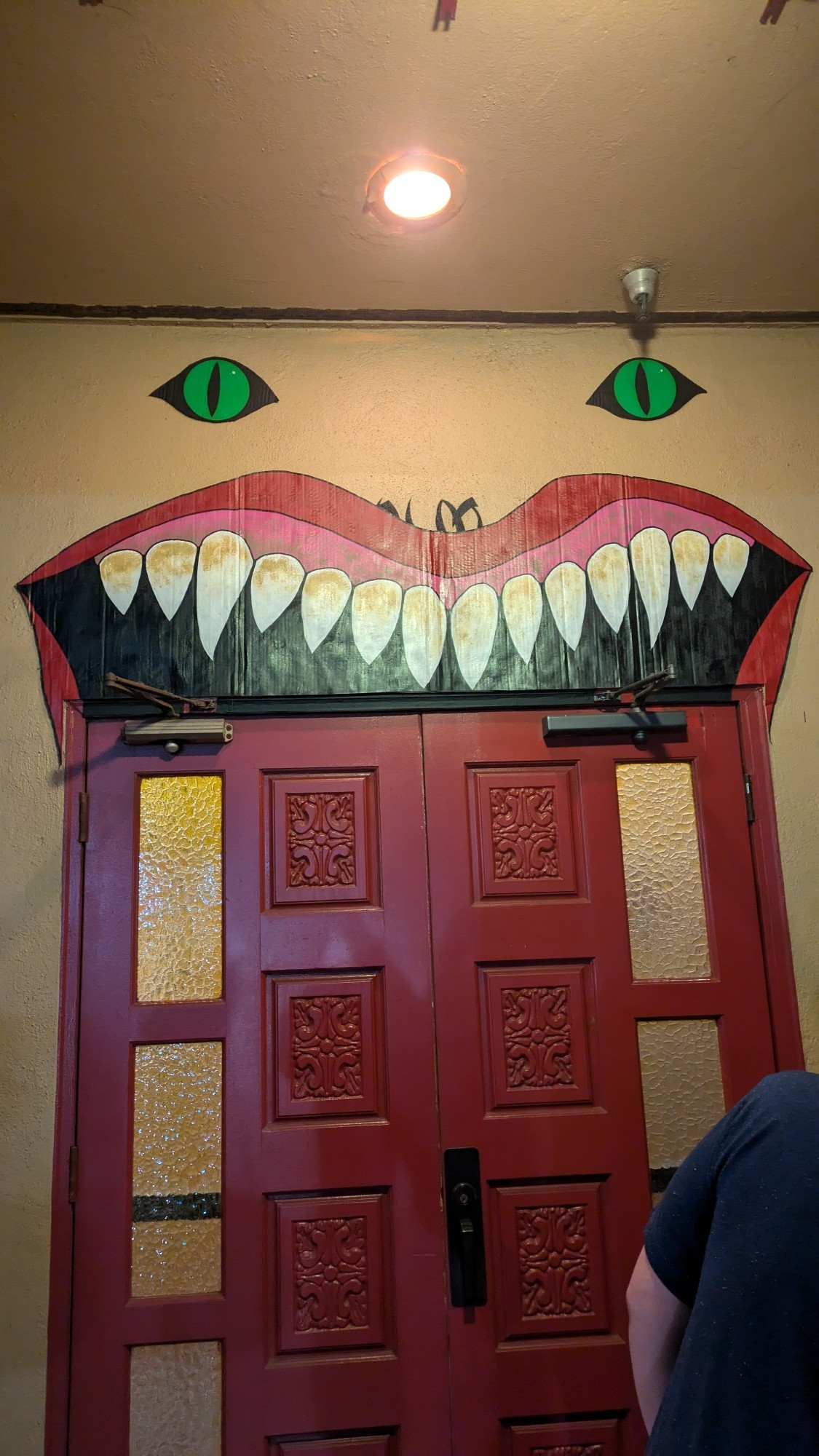 Two red doors topped by a giant evil fanged cartoon smile and two glowing green cat eyes, theming the Palm Theatre for House (1977)