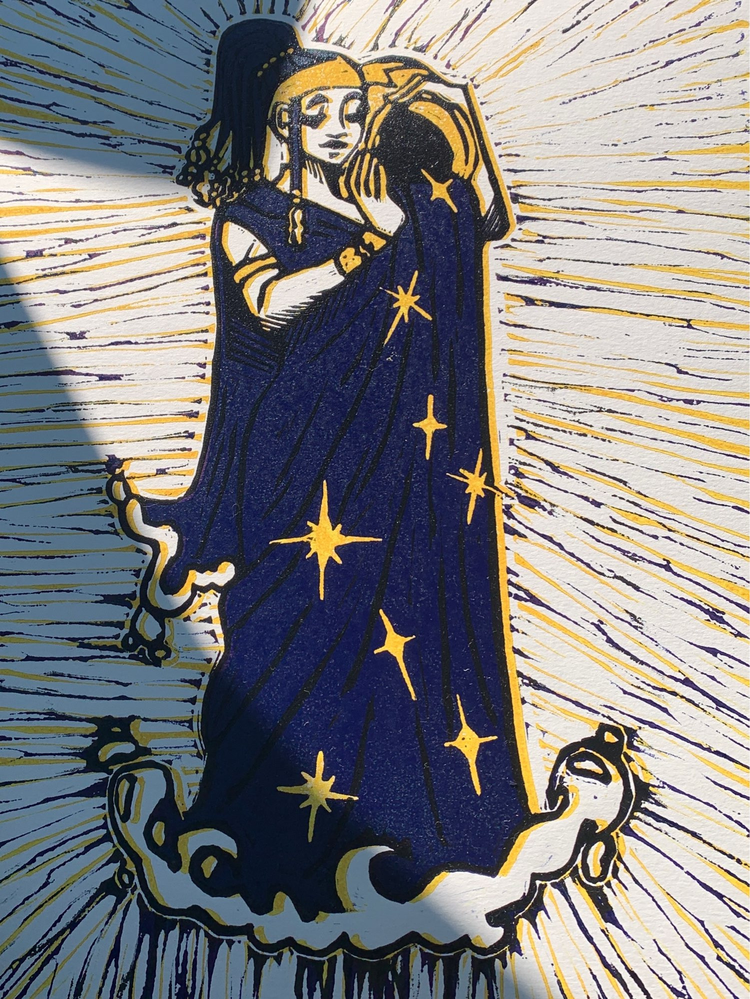 a photo of a relief block print. There is a single figure in the center, who is a representation of the zodiac sign Aquarius. she is holding a jar on her shoulder as water pours out, which then becomes her dress. yellow stars dot the dress.