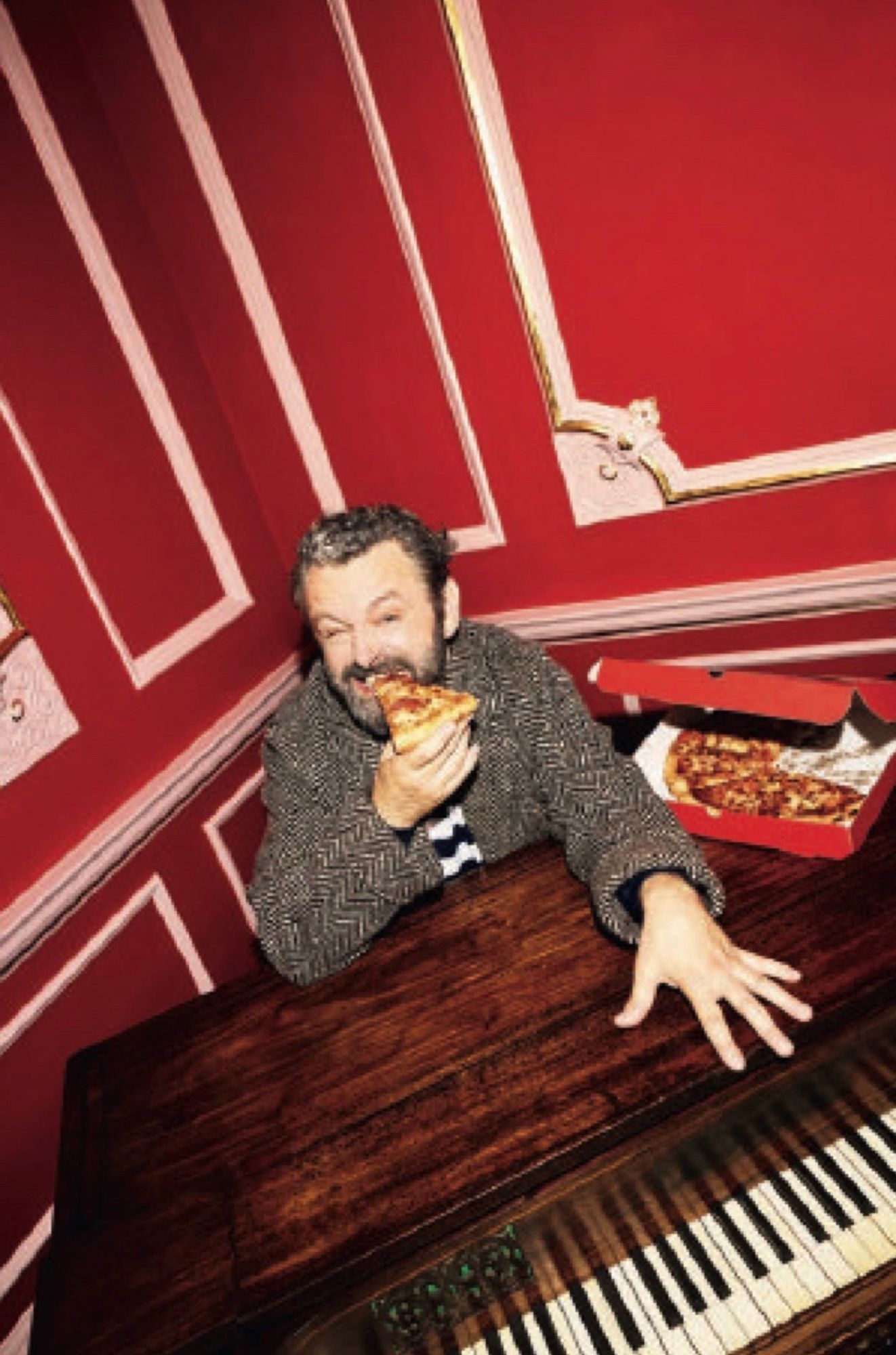 Michael Sheen eating pizza and using a piano as a table