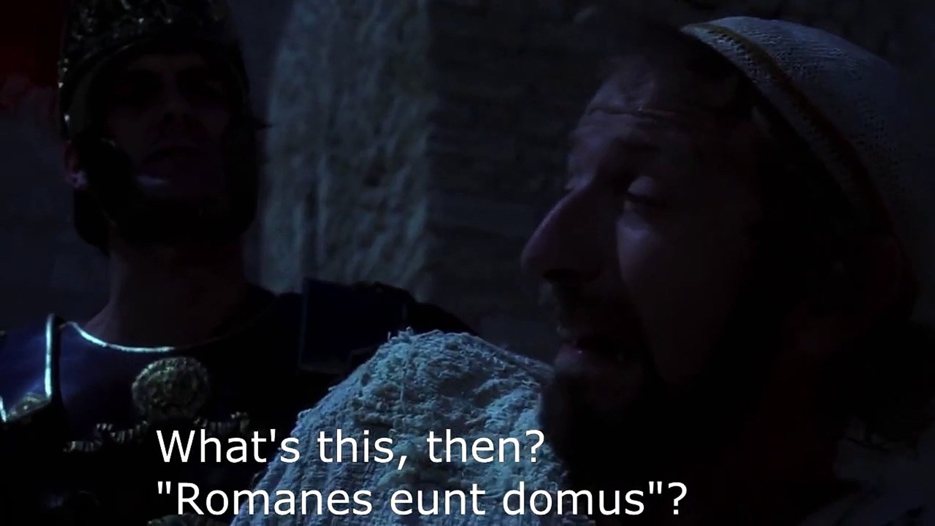 screenpic from film, ‘Monty Python’s The Life of Brian’ in which Brian (Graham Chapman) is being apprehended at night by a Roman centurion (John Cleese) while painting graffiti on the walls. The subtitle (Cleese) reads: “What’s this then? ‘Romanes eunt domus’?”