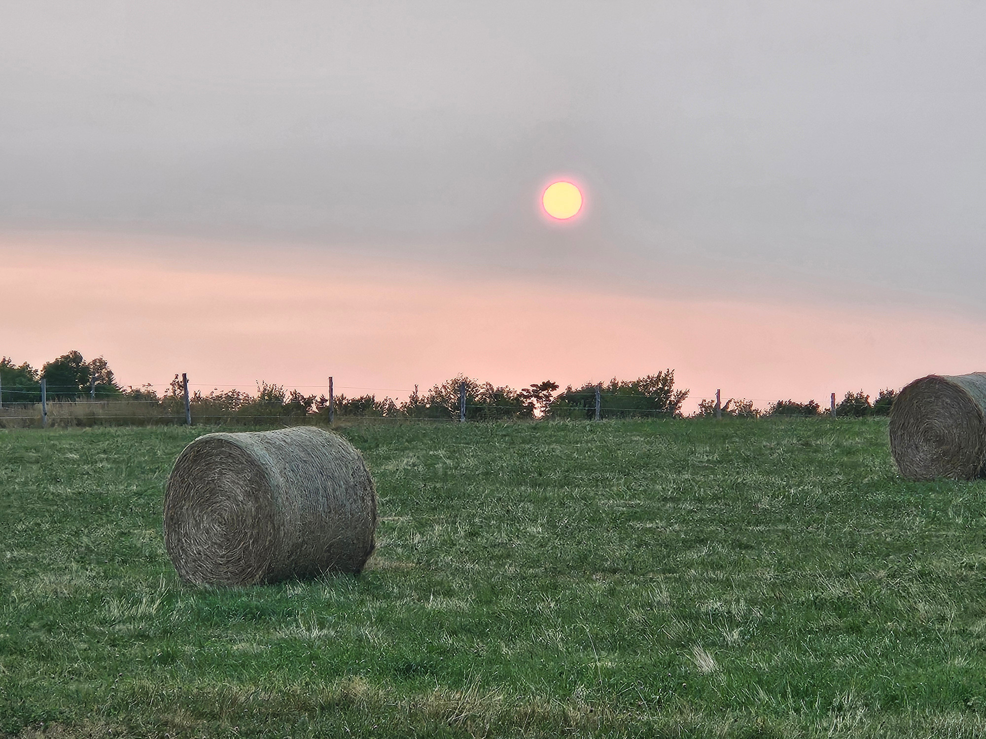 The sun low on the horizon with hay bales in the foreground.