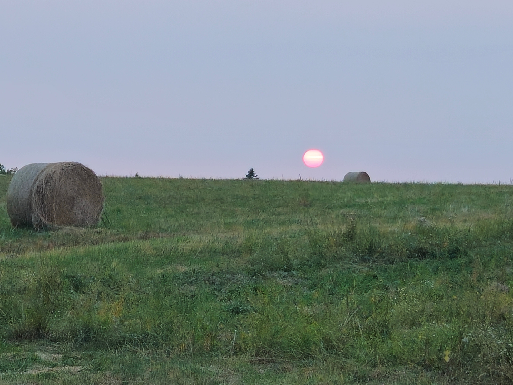 The red sun just over the horizon with bales of hay in the foreground.