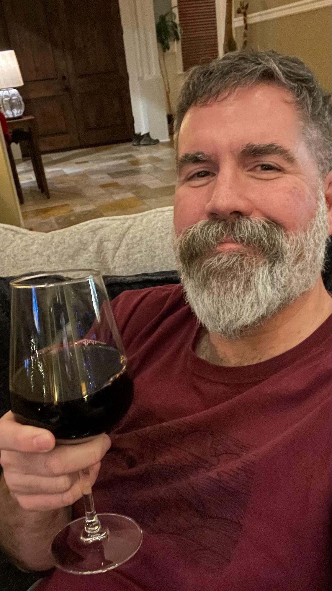 Bearded man in maroon shirt holding a glass of wine