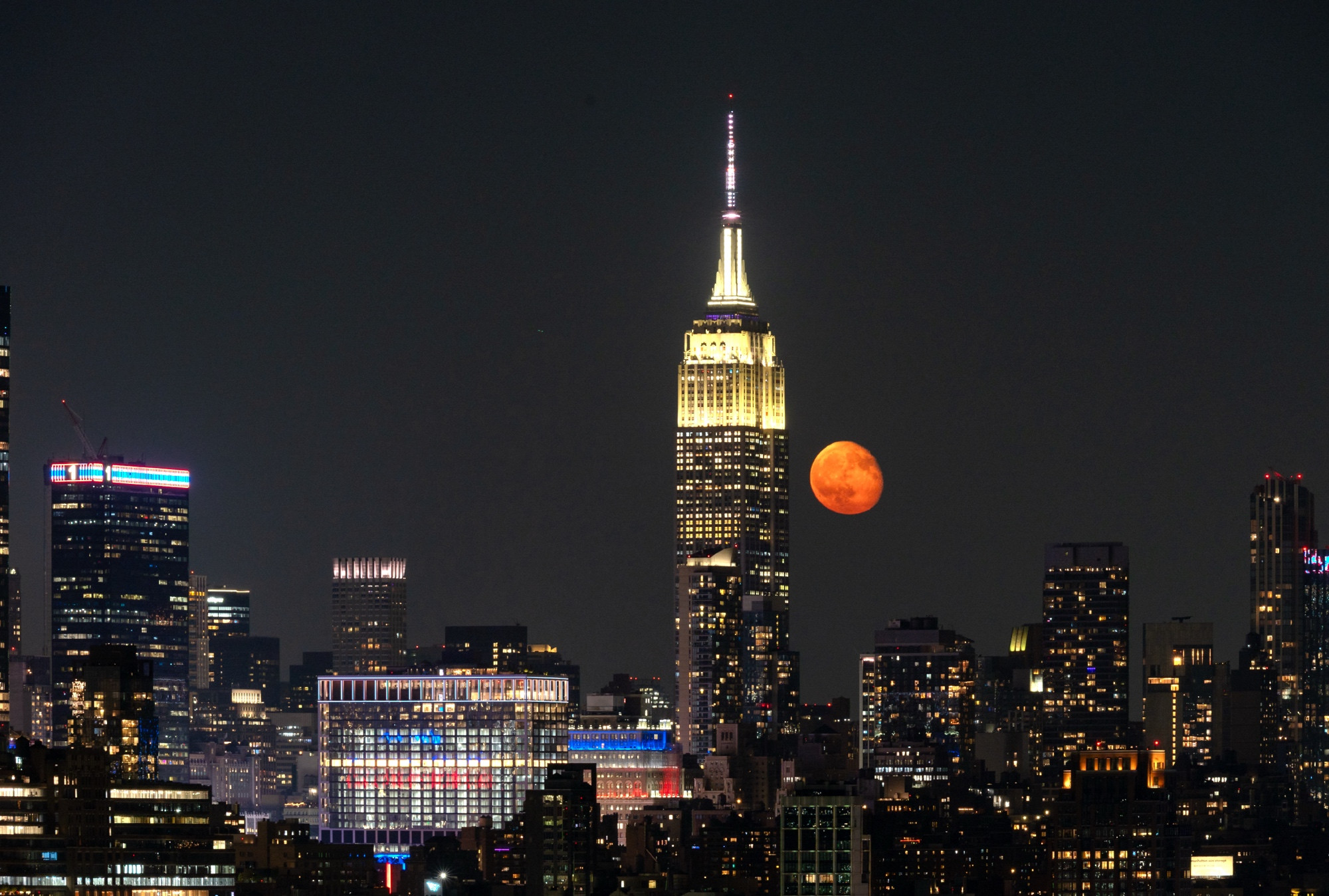 A vivid orange moon rises beside the mighty Empire State Building. 