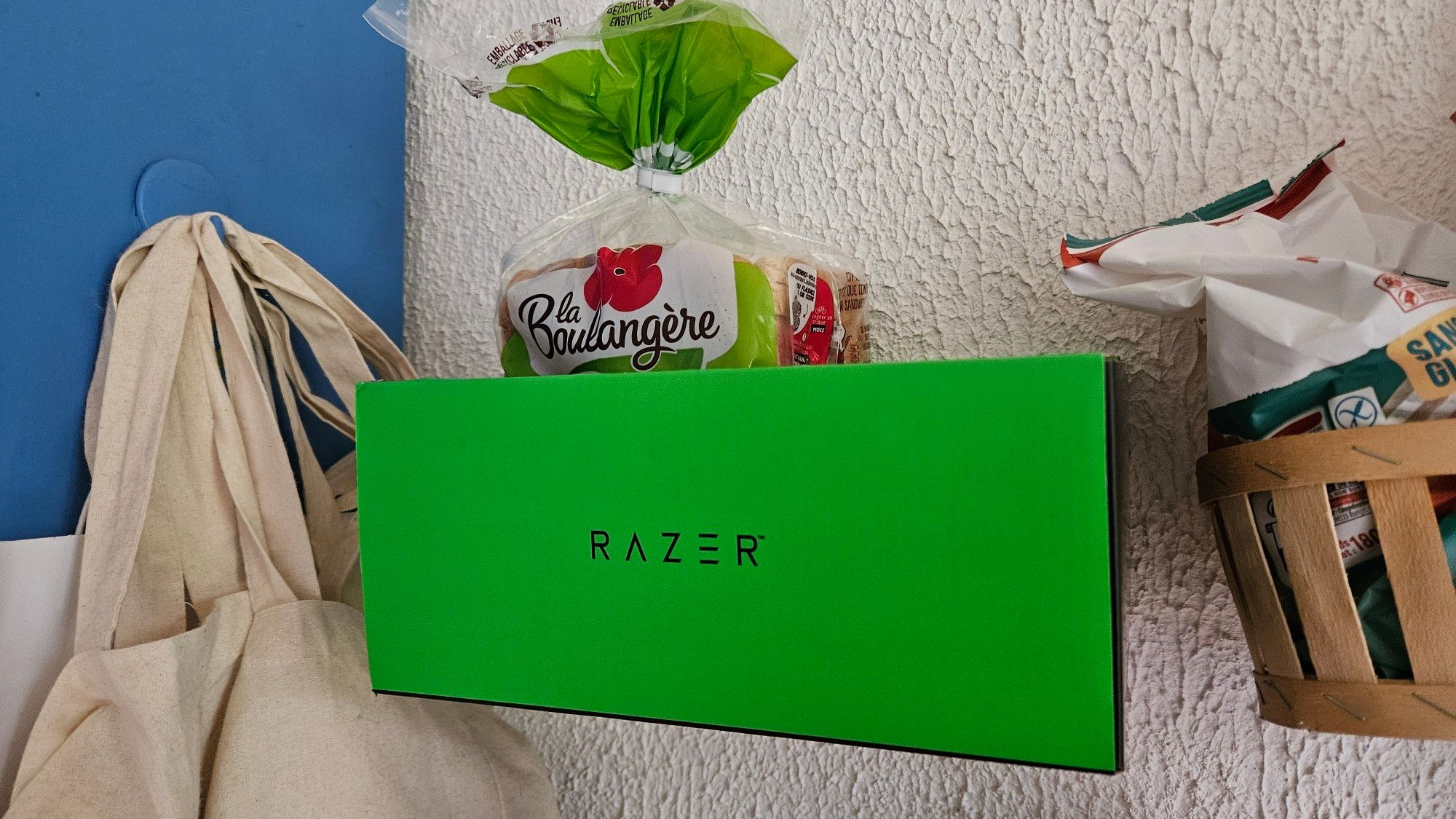 Une boite en carton verte et noire de la marque "Razer" est fixée sur un mur de cuisine blanc de manière à pouvoir servir à y poser un paquet de pain de mie.